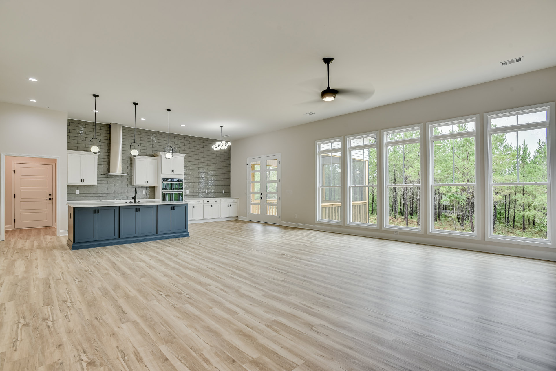 Spacious open room featuring wood flooring, white walls, ceiling fan, white cabinetry, kitchen counter with sink and faucet, white double doors with glass panels, and black door