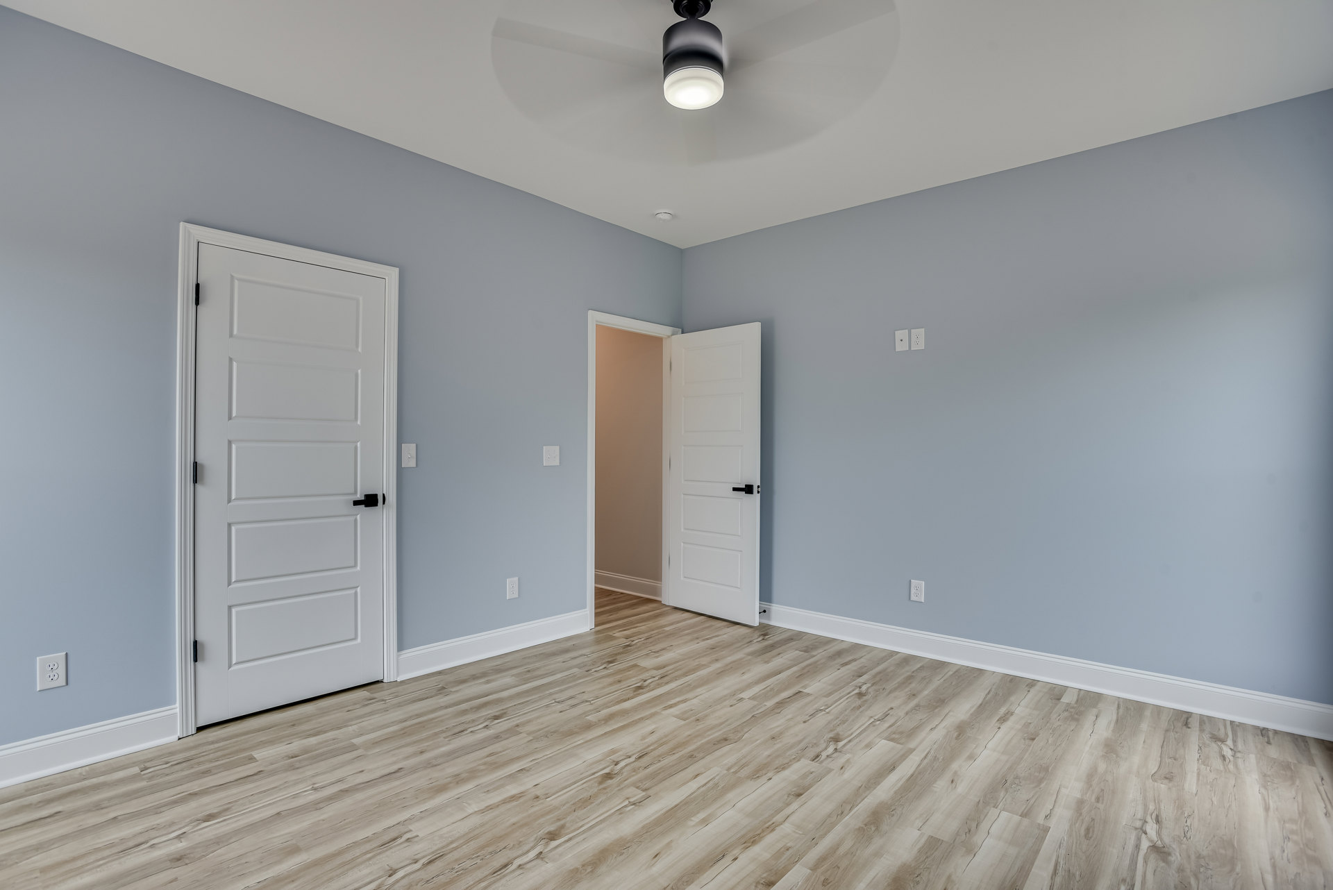 Wood flooring room with two white doors featuring black handles, ceiling fan with light fixture, neutral plaster walls, and white ceiling.