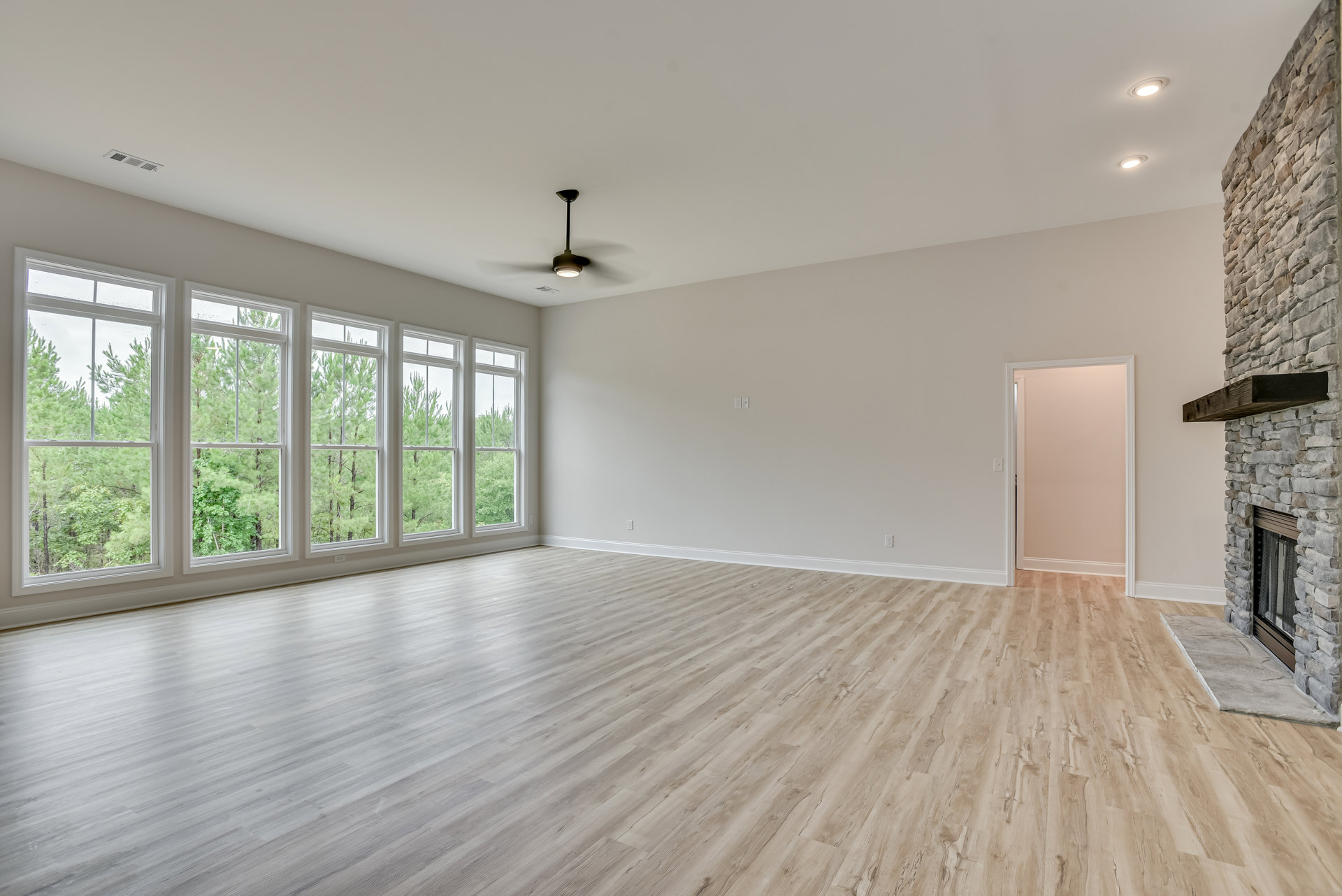 Spacious living area with wood flooring, multiple windows, ceiling fan, white door, and light pink accent wall