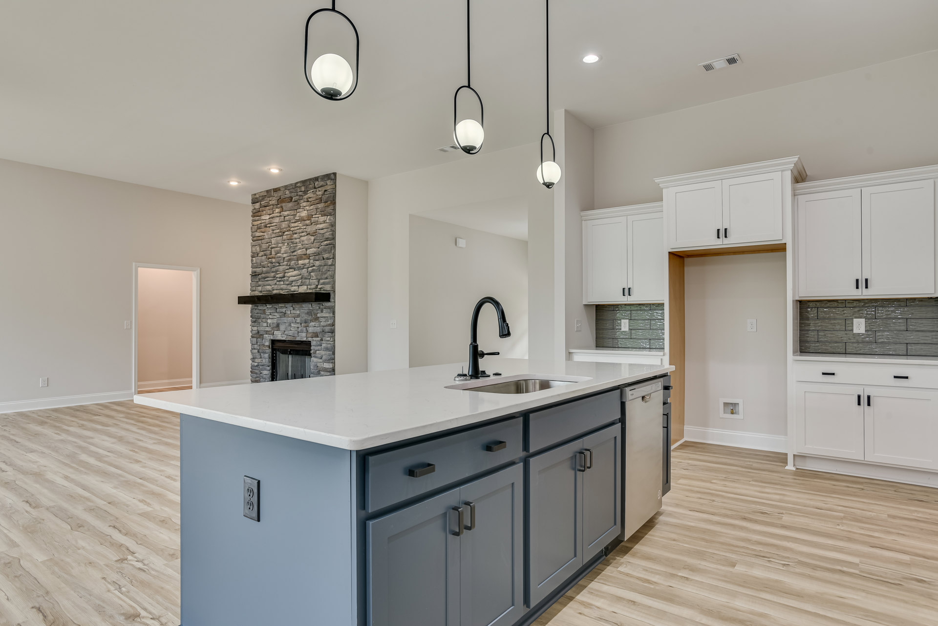 Quartz kitchen island with built-in sink and cooktop, black faucet, white cabinetry, stone accent wall, wood shelving, light hardwood flooring, and pink wall near white door frame