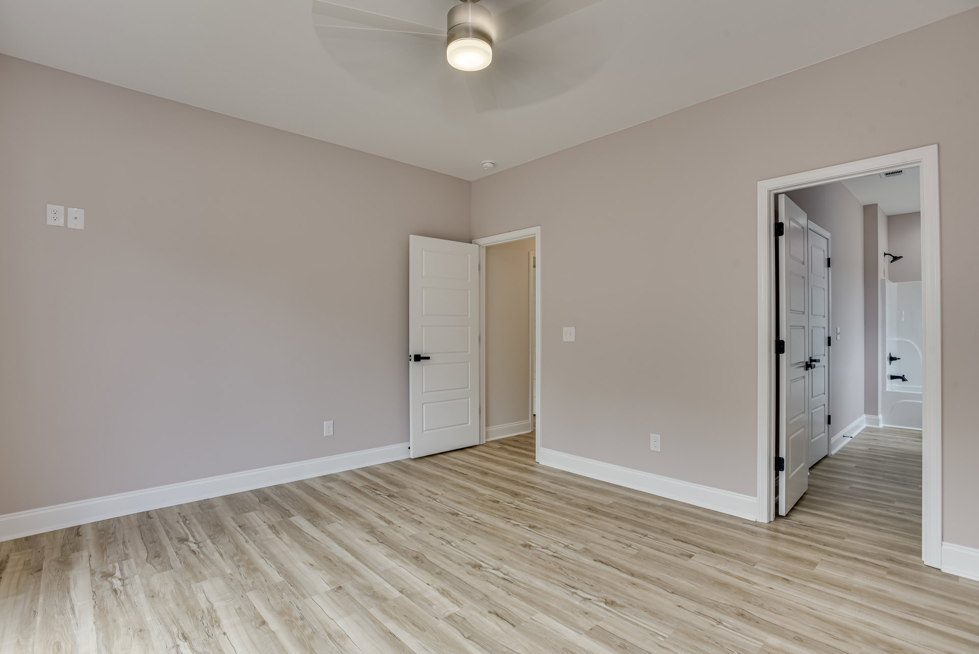 Wood flooring in a bright room with white paneled doors, black handles, and a ceiling fan mounted on a plaster ceiling