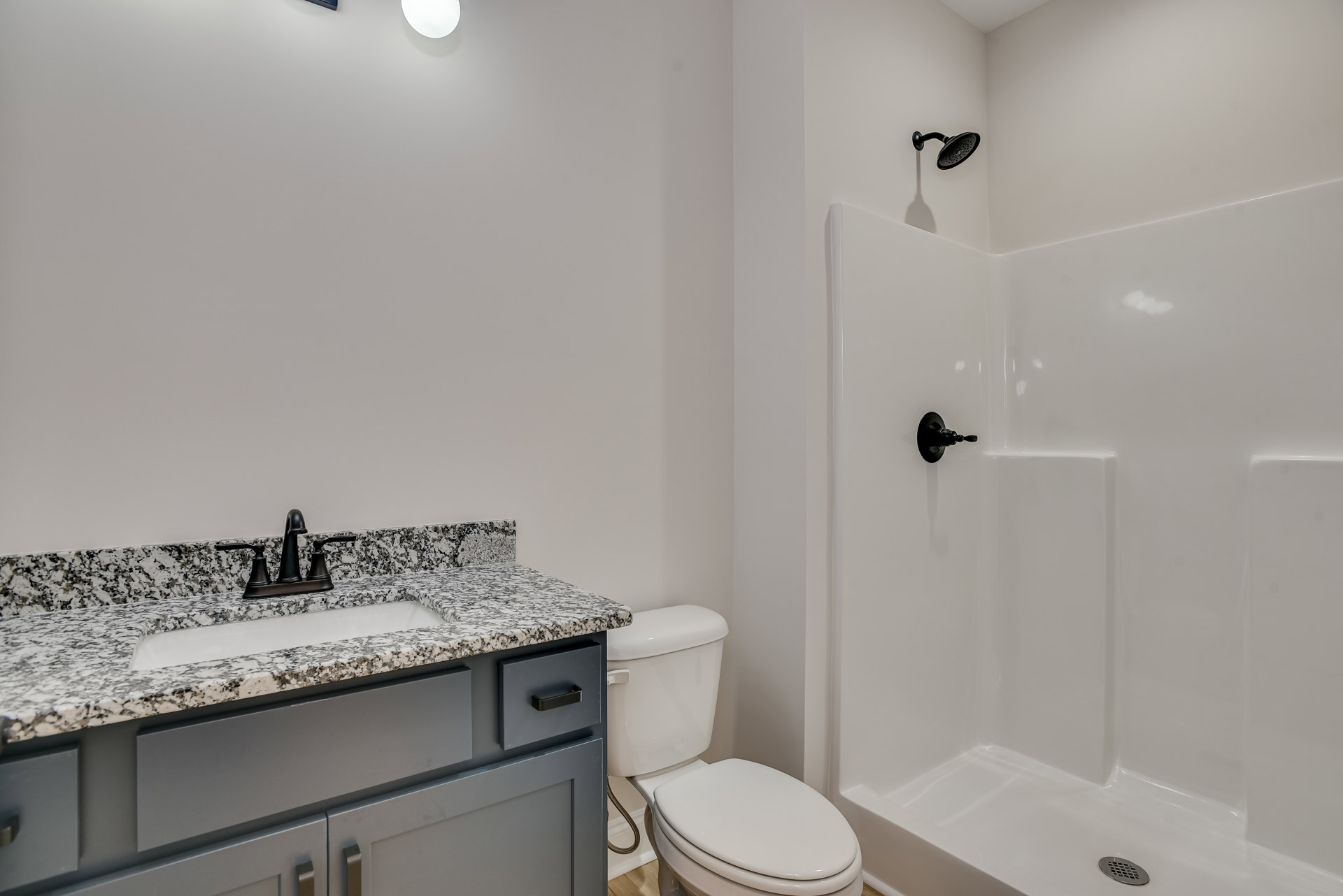 Modern bathroom featuring a white porcelain sink with chrome faucet, glass-enclosed shower with round showerhead, white toilet with lid up, light tile flooring, and white