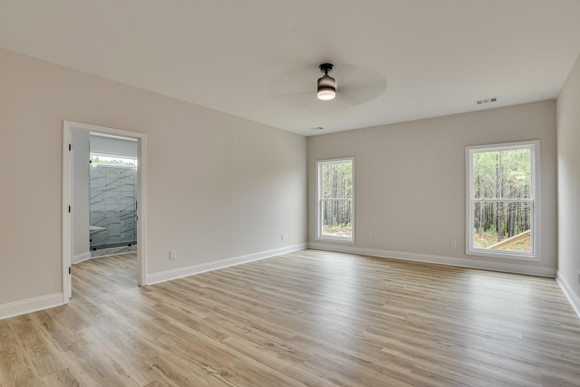 Wood-floored room featuring a ceiling fan, large window with tree views, white tile shower wall with black grout lines, and modern light fixture