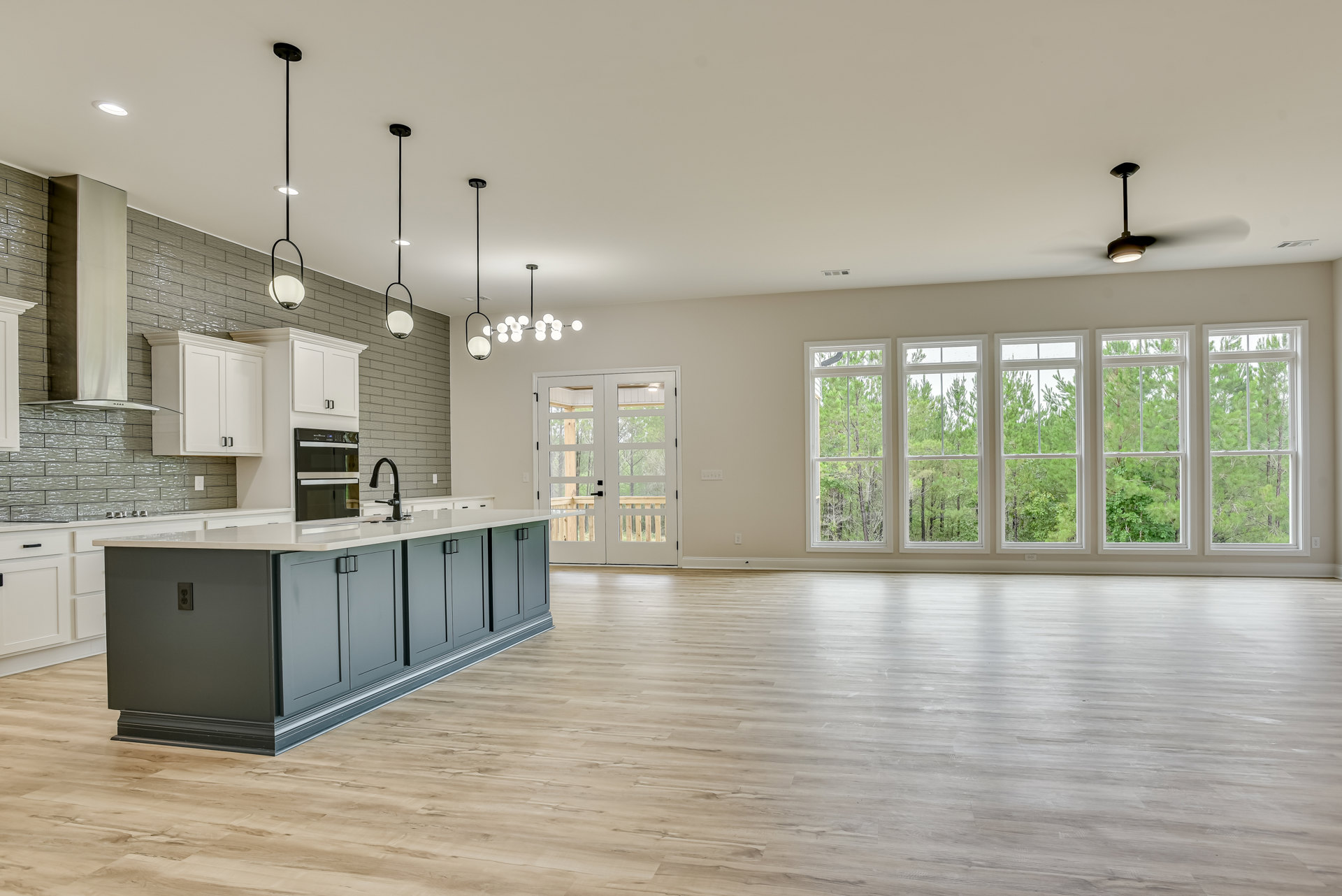 Spacious kitchen with wood flooring, central island featuring sink and built-in microwave, glass-paneled double doors, multiple windows, and white cabinetry