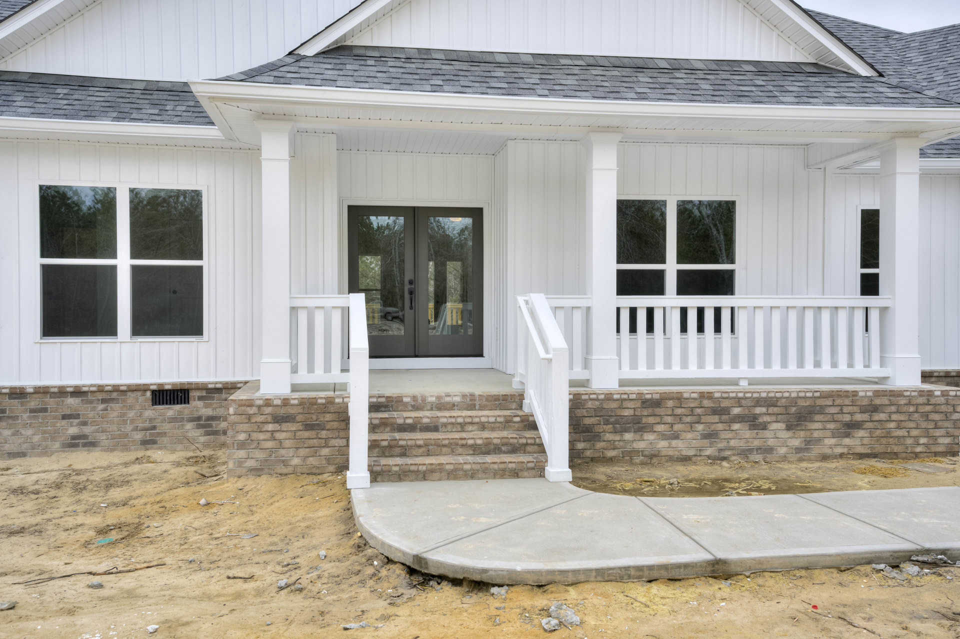 Front porch with white railings, double glass doors, white pillars, concrete steps, and a window with white trim; brick wall and parked car visible in background