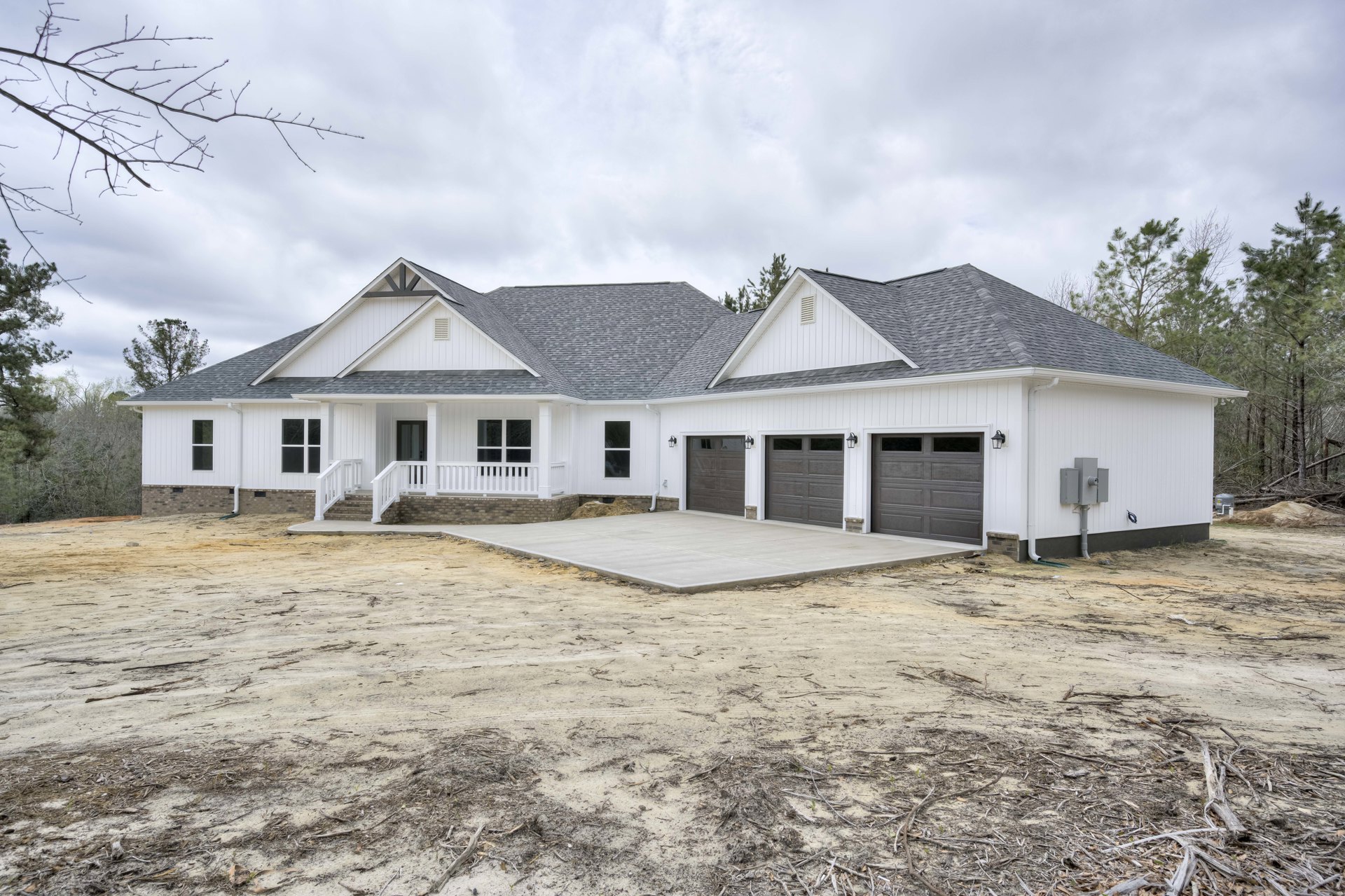 Two-story home with gray siding, white trim, attached garage featuring windowed door, concrete driveway, gable roof, and landscaped front yard with trees.