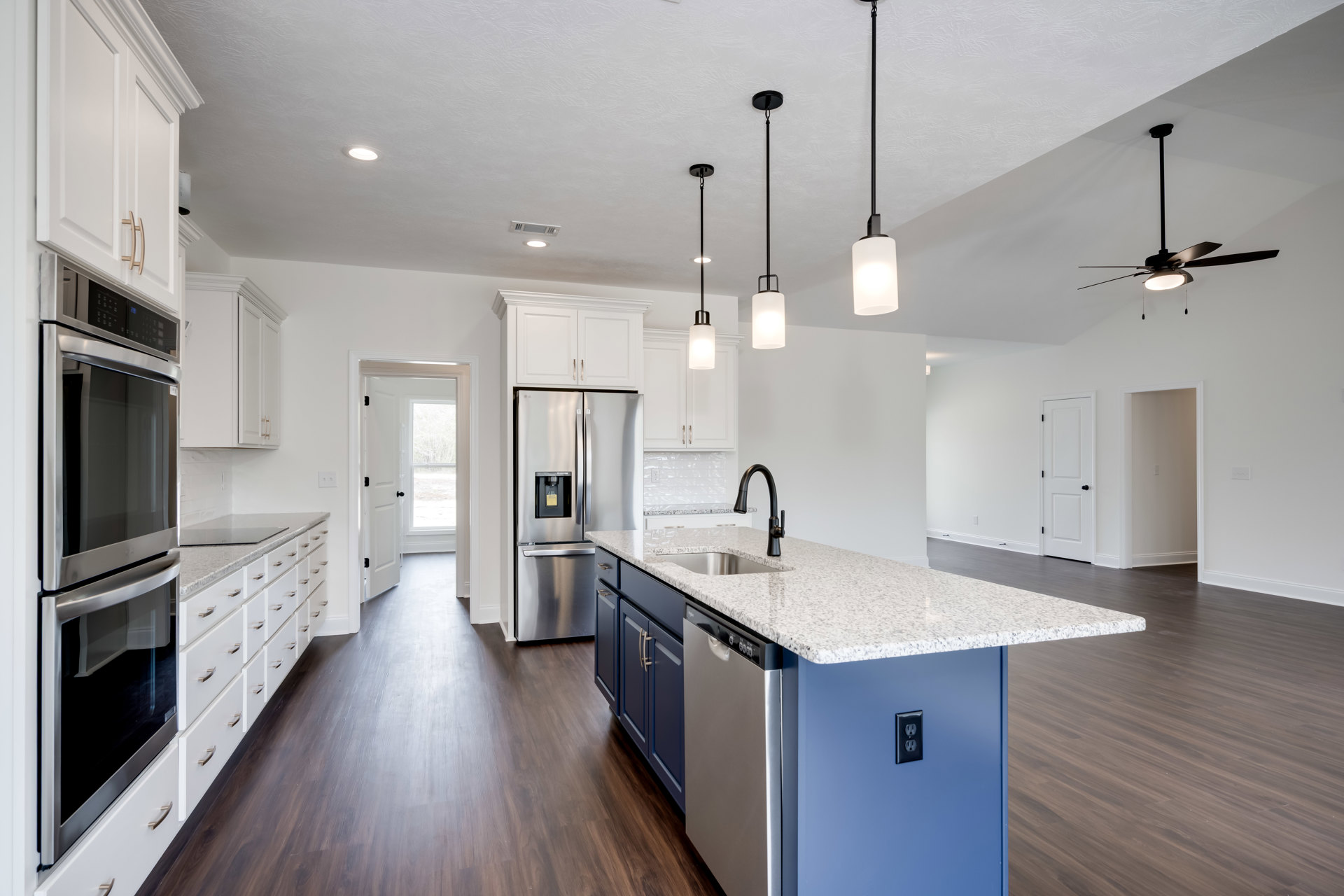 Blue kitchen island with quartz countertop, stainless steel oven and refrigerator, white cabinetry, tile backsplash, and pendant lighting