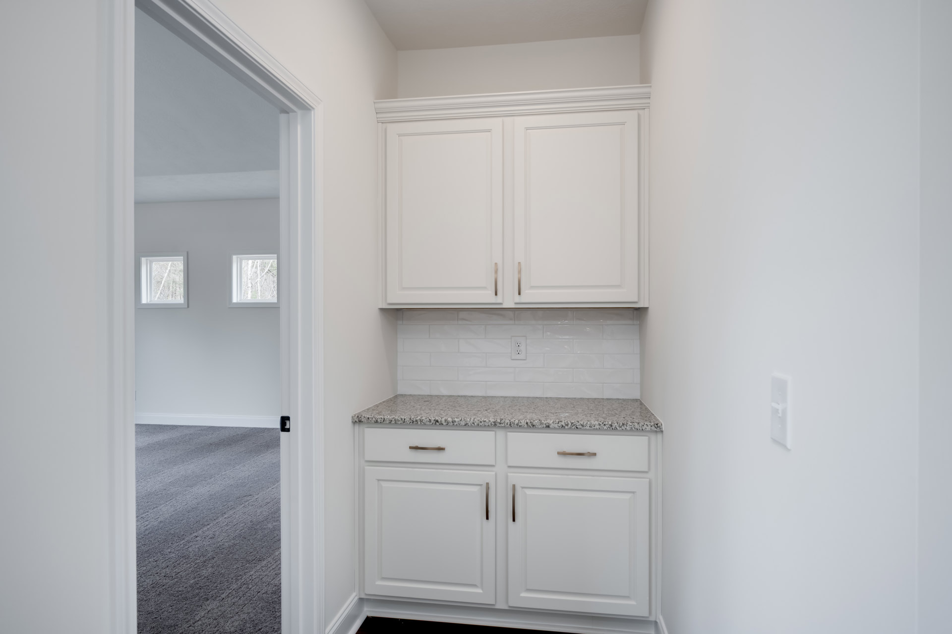 White kitchen cabinets with gold handles and marble countertops, white door with gold handle and wooden frame, stainless steel sink, light walls, and built-in appliances.