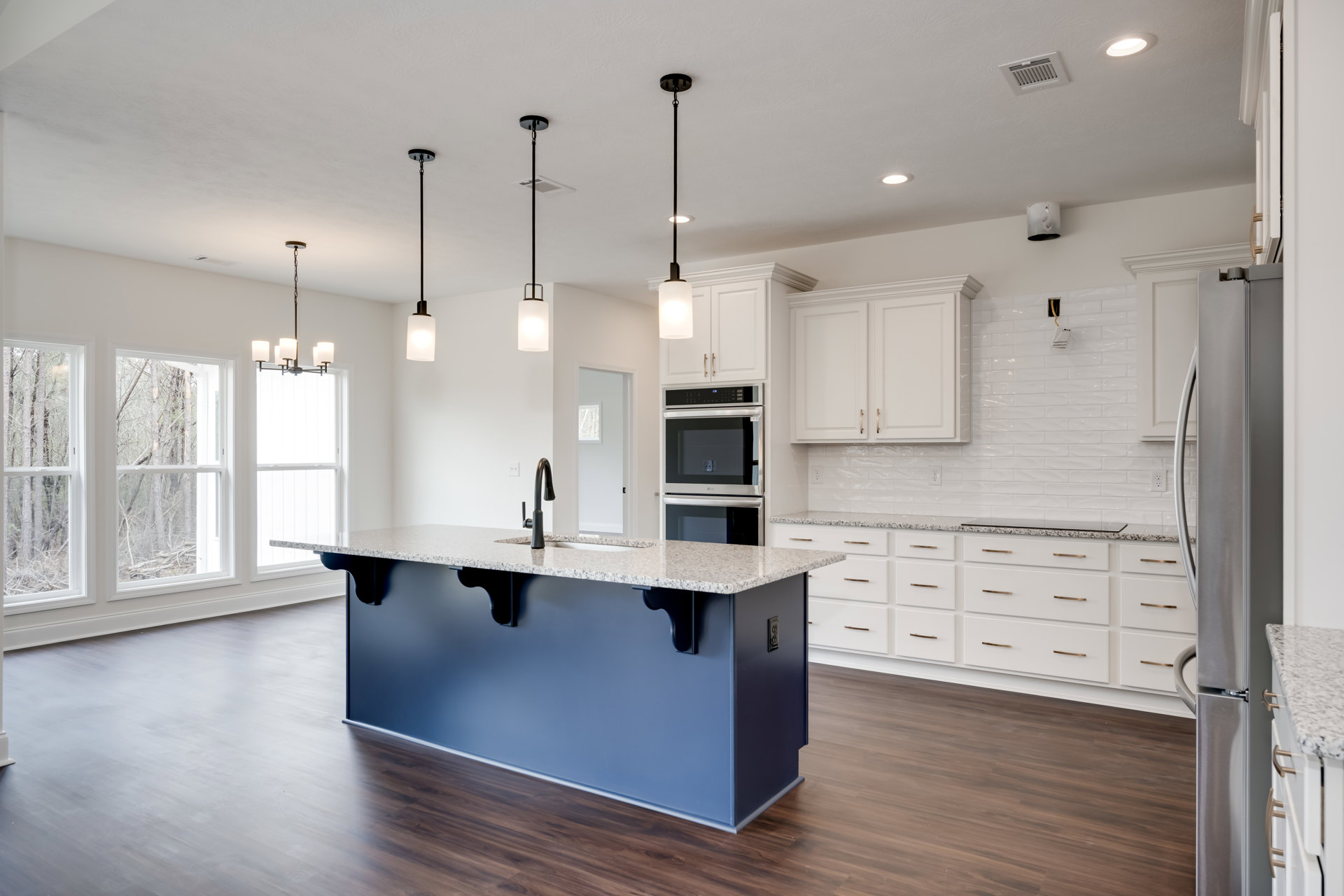 Kitchen with white shaker cabinets, central island with light stone countertop, stainless steel oven, pendant light fixtures, and hardwood flooring