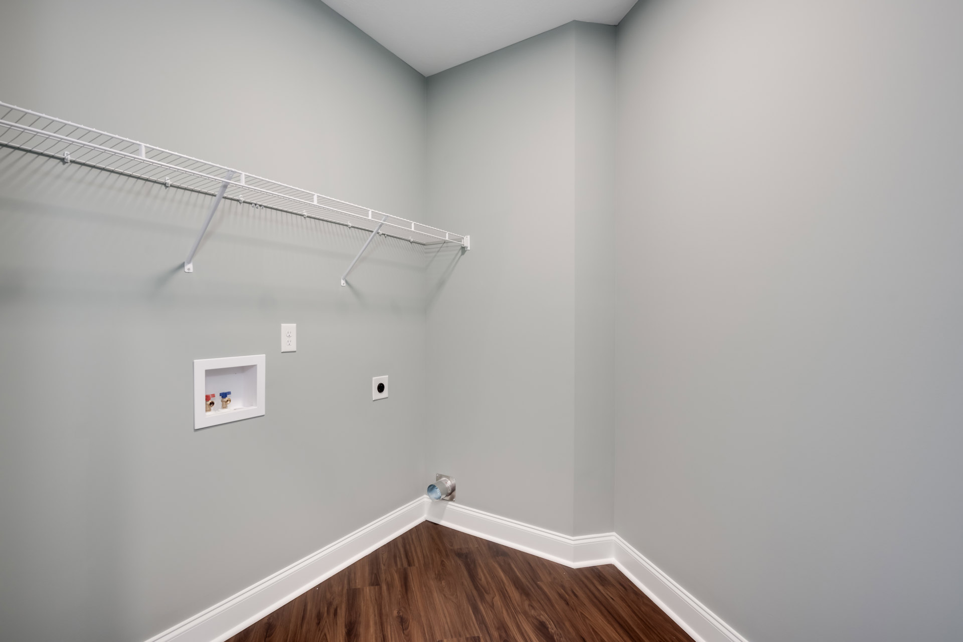 Wood floor with white baseboard, white wall-mounted shelf, white plaster walls, ceiling fan, and wall vent in a residential room
