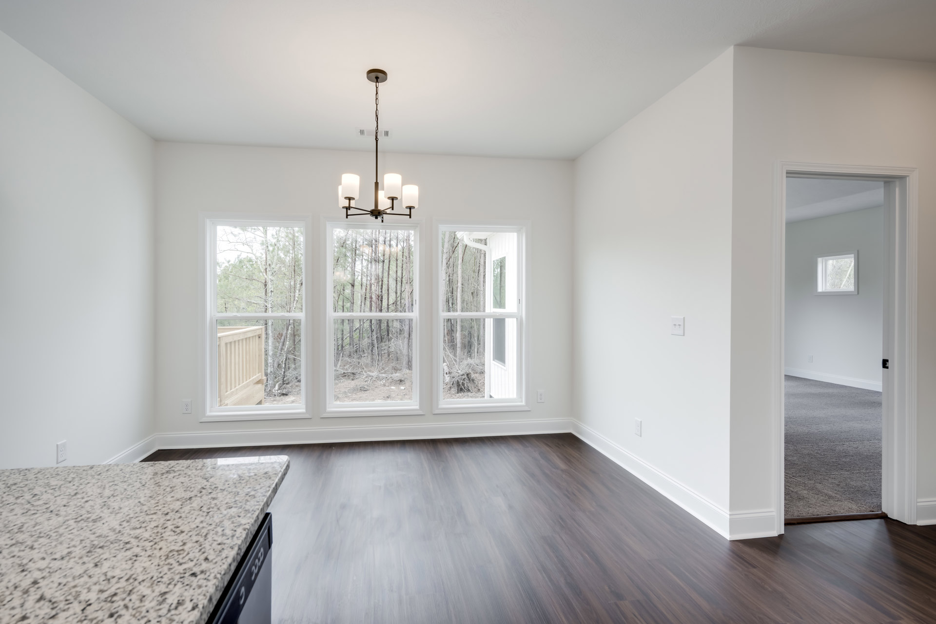 Marble countertop with black and white speckled surface, wood panel cabinetry, chandelier hanging from ceiling, windows with view of trees, light-colored laminate flooring, plaster