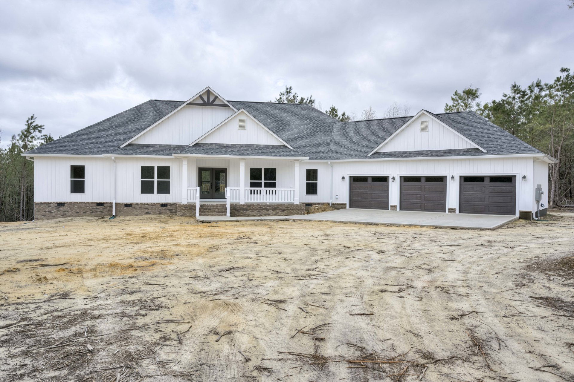 White house with grey roof, double glass doors, white railing, and dirt yard under cloudy sky