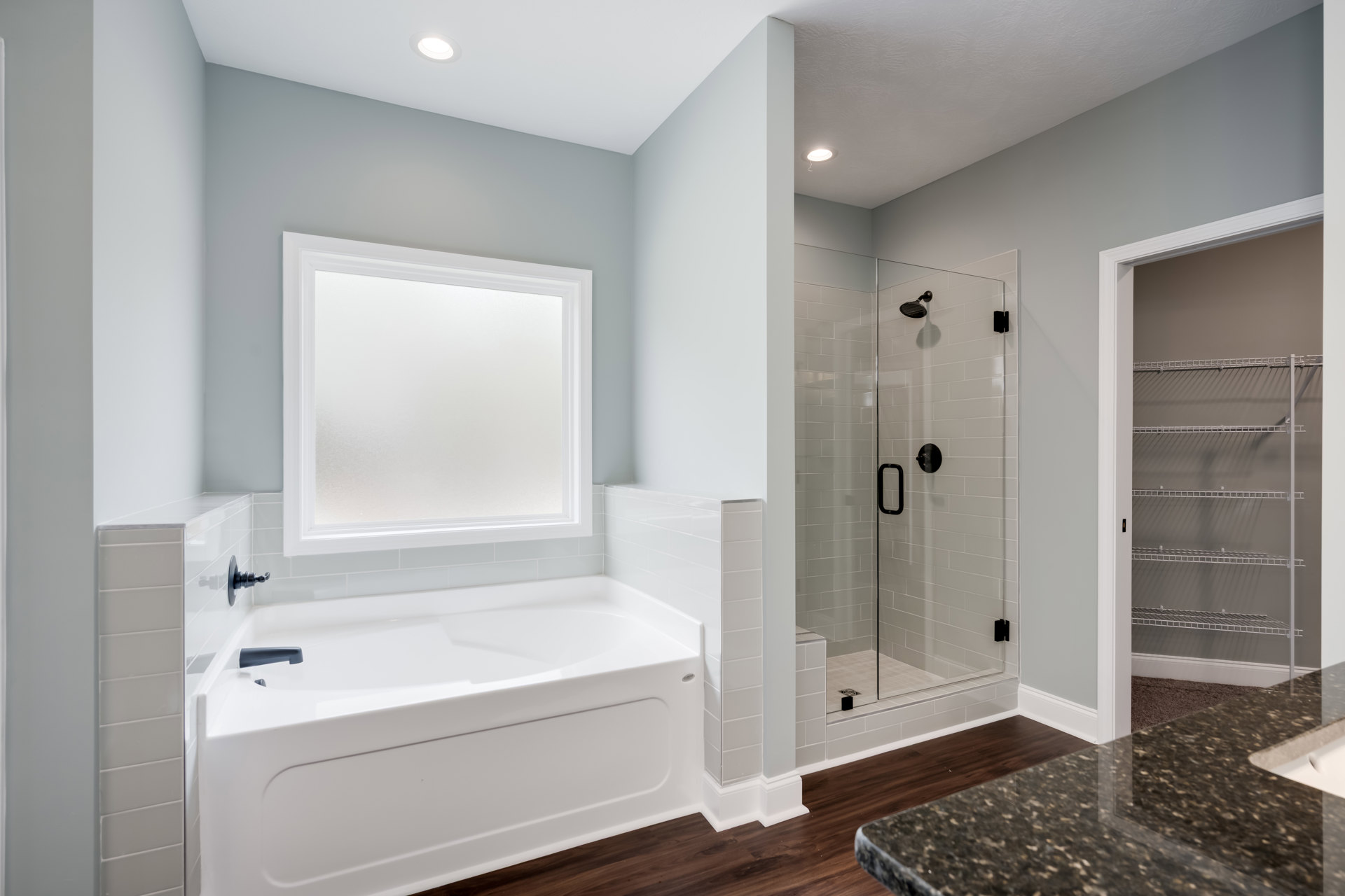 Bathroom featuring a freestanding white bathtub with blue faucet, glass-enclosed shower, marble countertop, tiled floor, and white cabinetry.