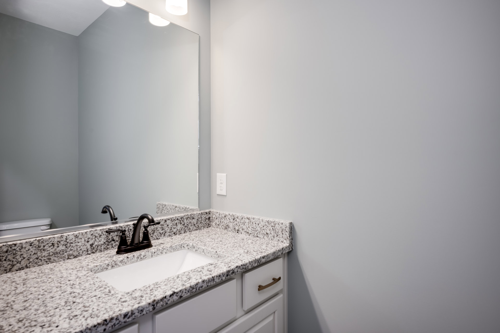 Marble countertop with black faucet, rectangular sink, white wall, black-framed mirror, and brown cabinet handle