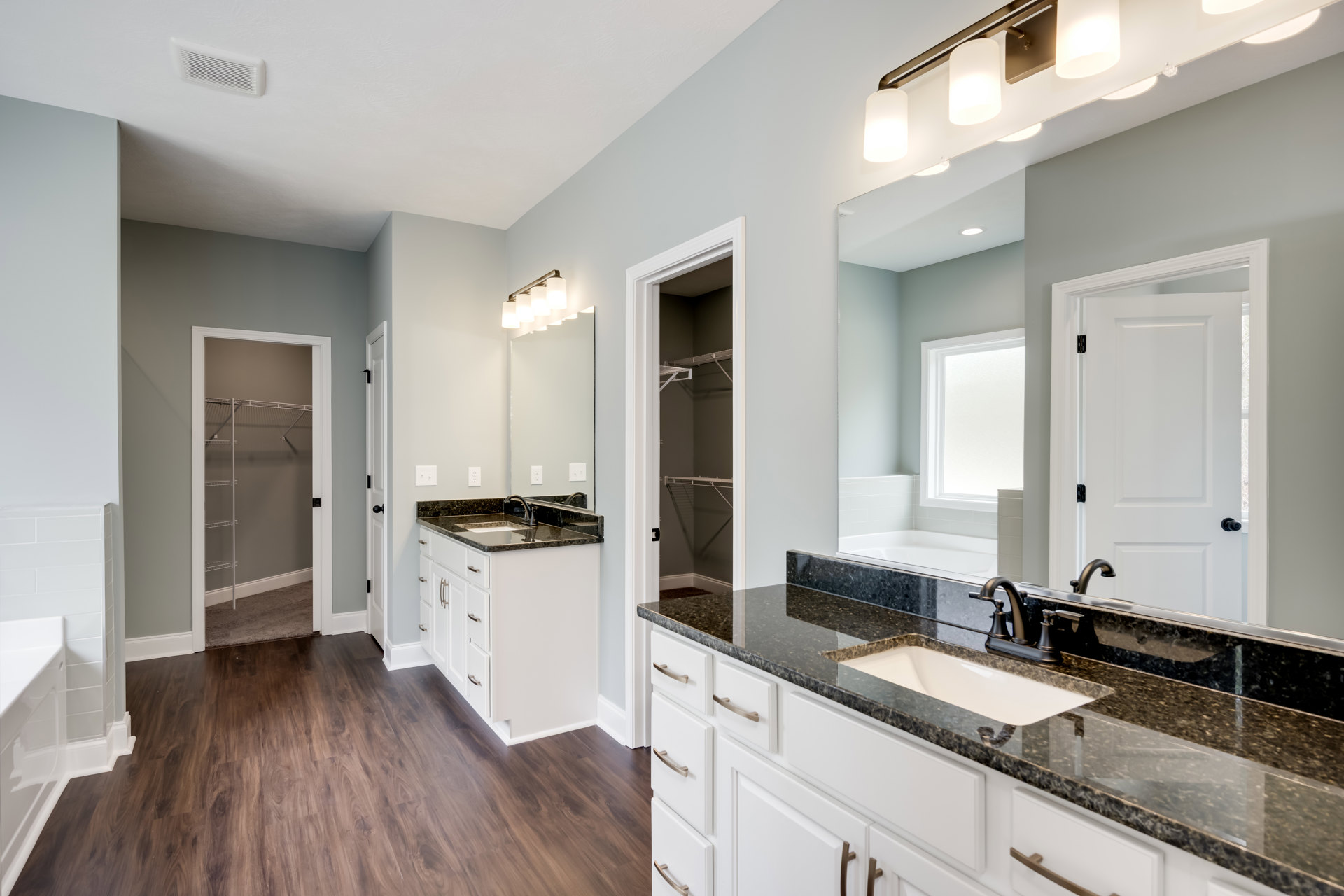 Bathroom with white cabinetry, black countertops, undermount sink with chrome faucet, wood flooring, open shelving, and white-framed window.