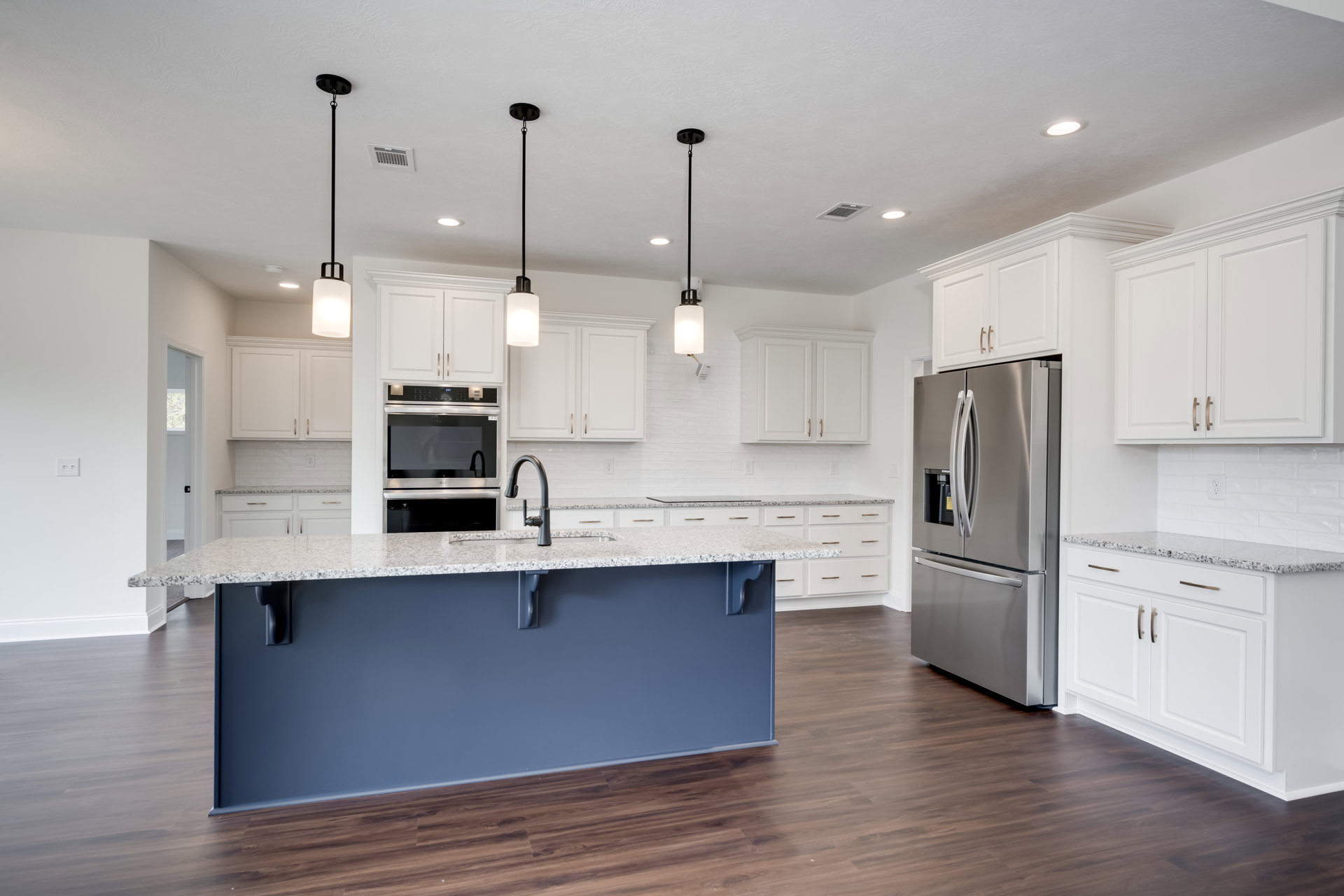 Spacious kitchen featuring a large quartz island, stainless steel refrigerator, oven, and microwave, white cabinetry, undermount sink, and light wood flooring