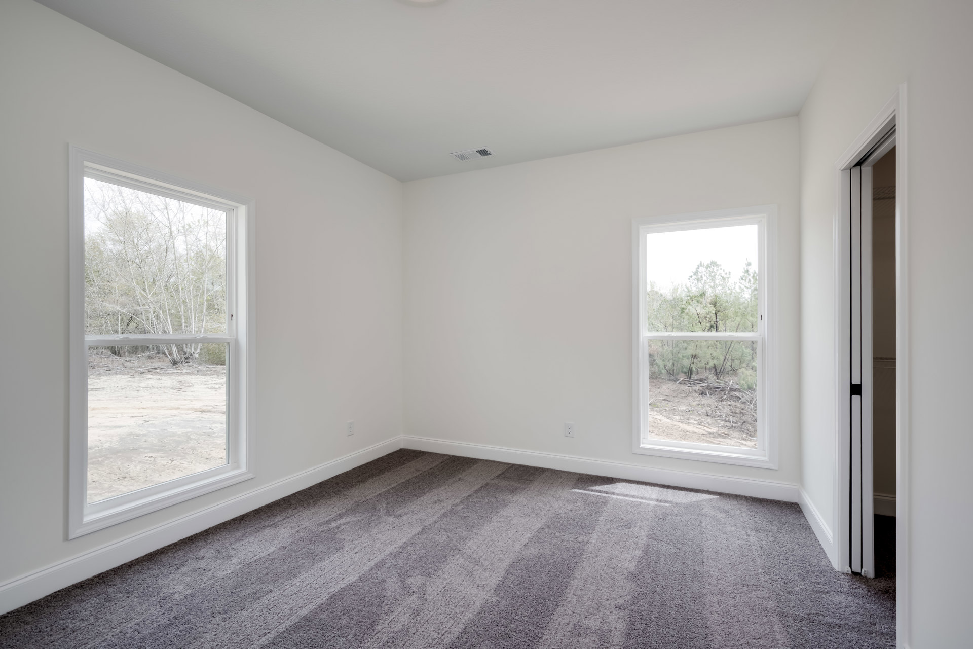 Bright carpeted room with large windows, white walls, and views of green trees outside