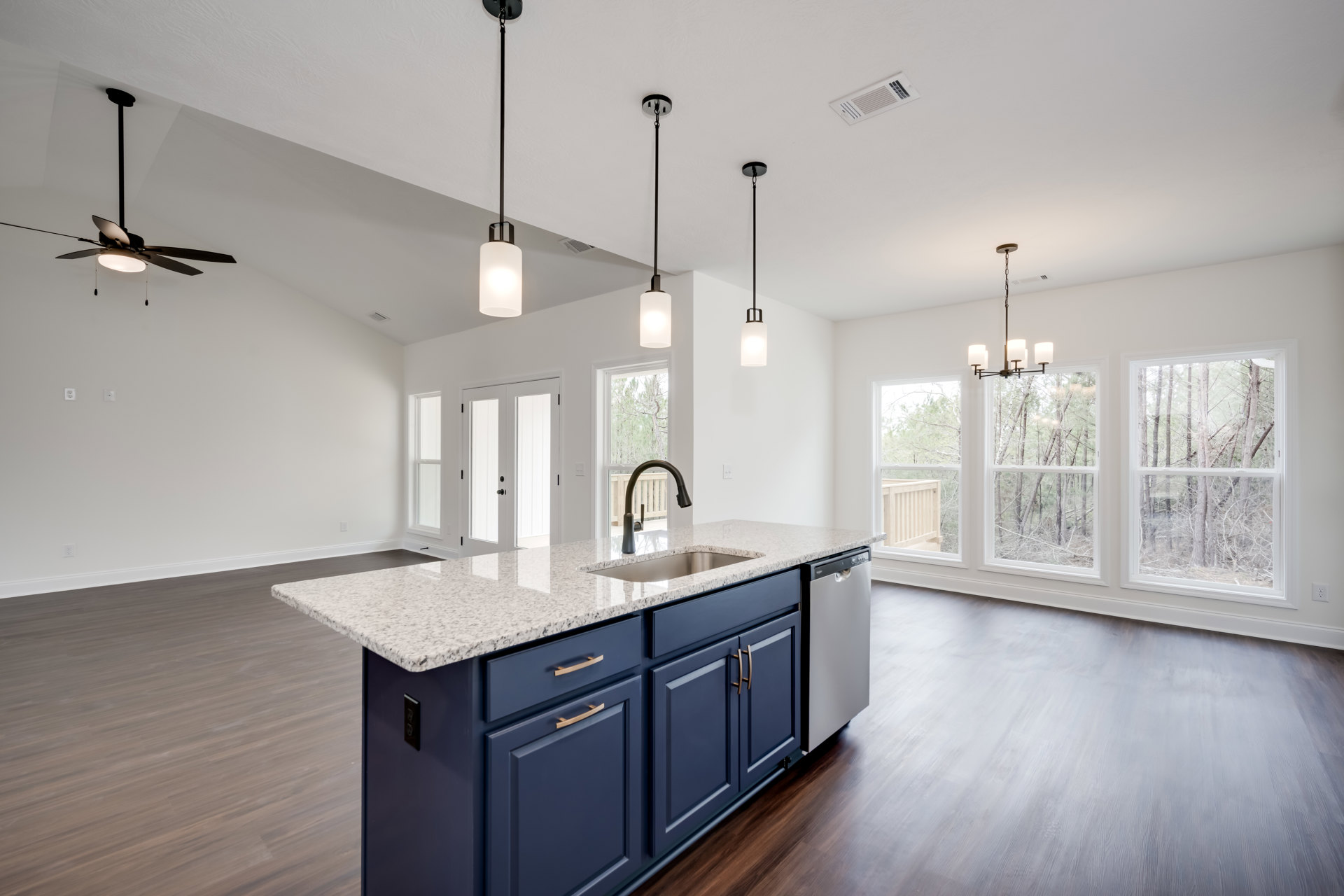 Kitchen with marble island, wood flooring, large window overlooking trees, white cabinetry, stainless steel sink, and granite countertops