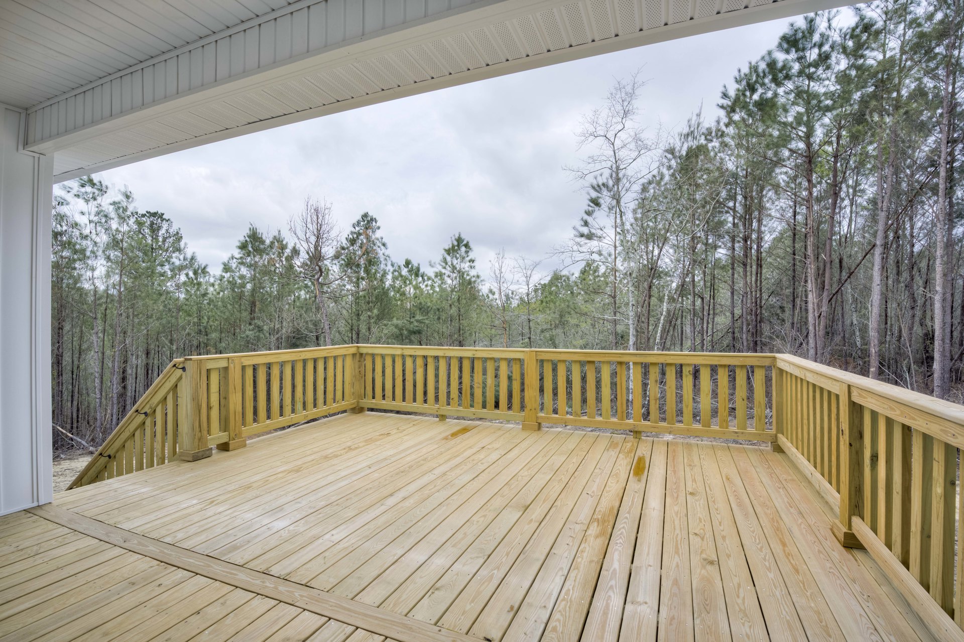 Wooden deck with railing overlooking leafy trees, outdoor space with balusters and fence