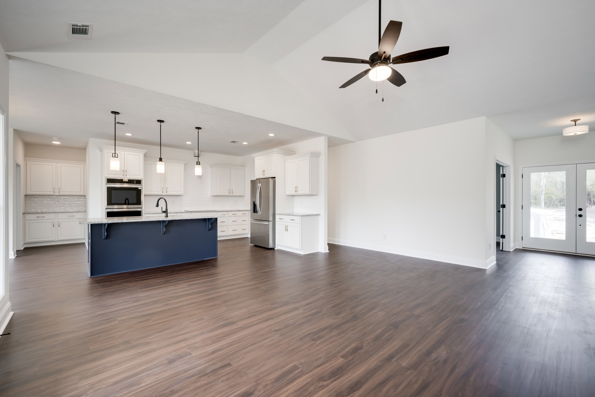 Spacious kitchen with hardwood flooring, ceiling fan with light, open silver refrigerator, sink set in countertop, and white door with glass panels