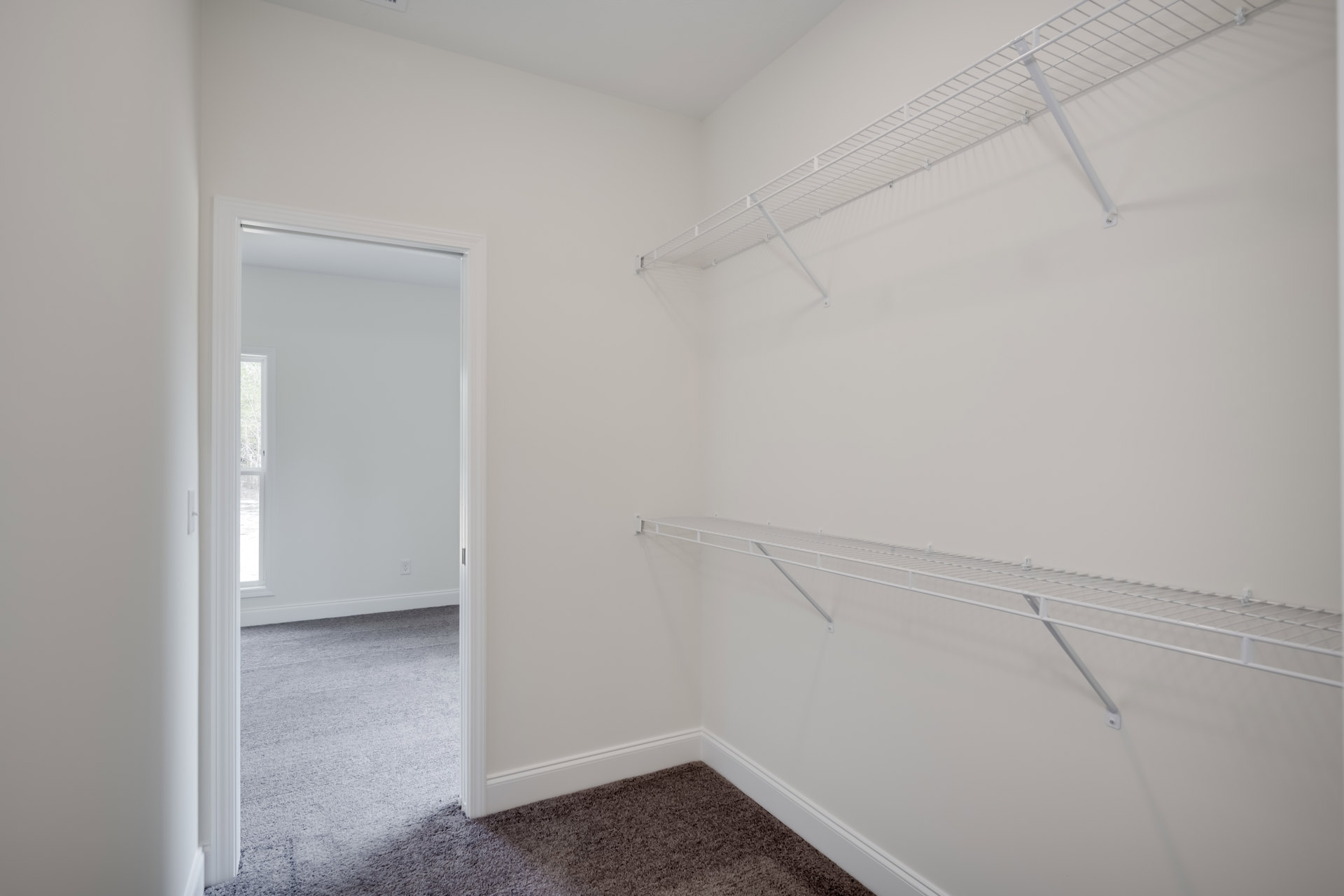 White built-in shelves on a wall, light carpet flooring, white walls and ceiling, open door leading to adjacent room.