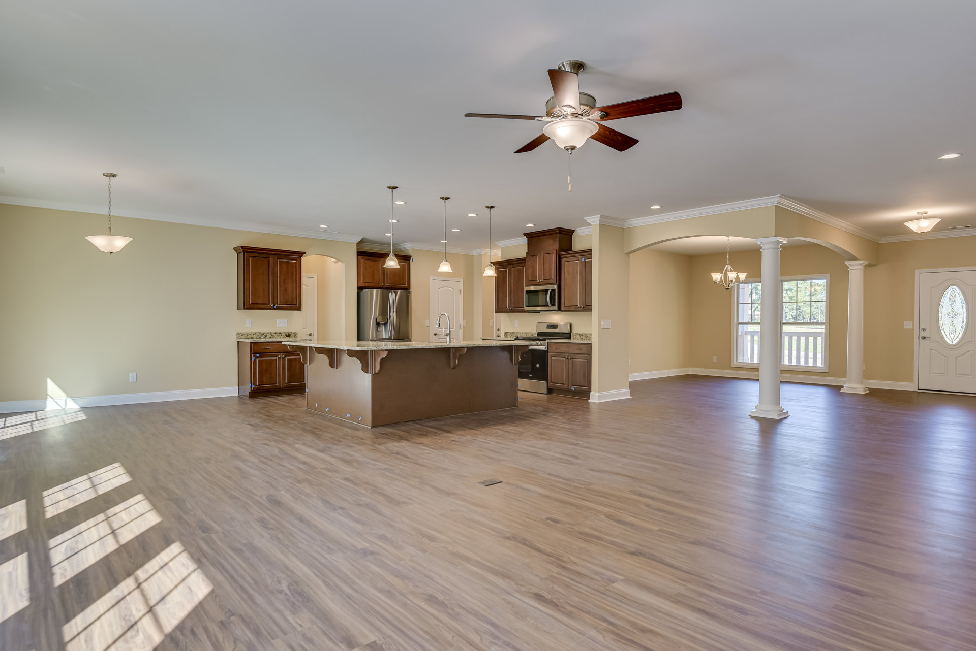 Spacious open floor plan featuring hardwood flooring, central kitchen island with stone countertop, stainless steel refrigerator with water dispenser, white door with stained glass