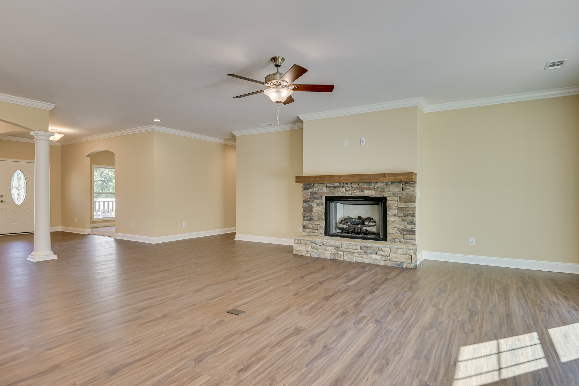 Living room with hardwood flooring, white plaster walls, ceiling fan with light fixture, and a fireplace stacked with logs