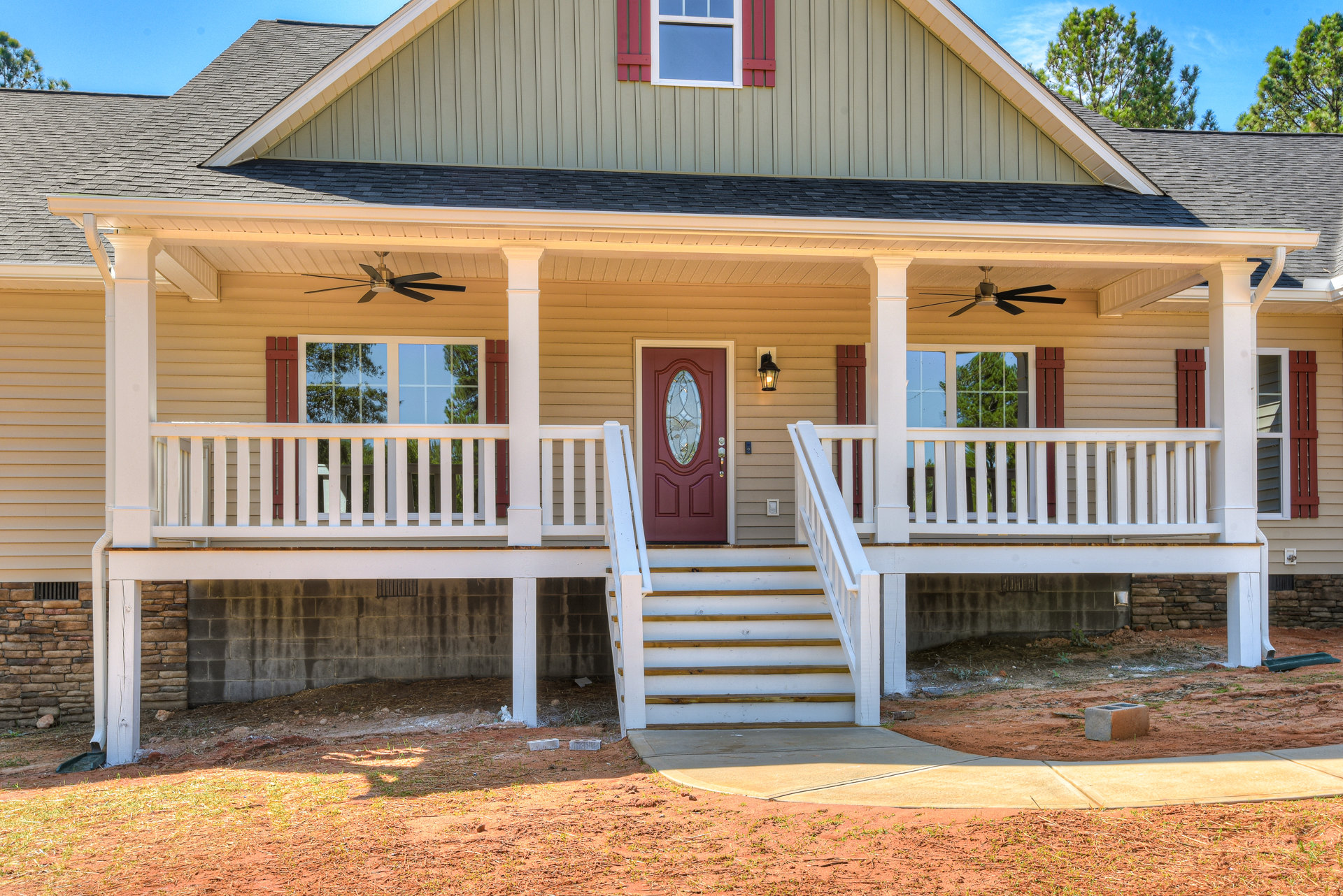White siding house with red front door, glass windows, and covered porch featuring white railing and wooden stairs
