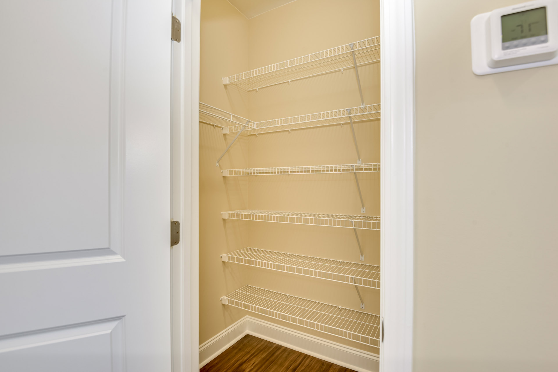 Walk-in closet with white built-in shelves, wood flooring, white baseboards, and a partially visible door