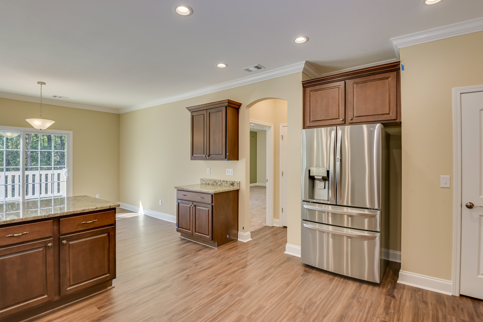Kitchen with stainless steel refrigerator featuring water dispenser, marble-topped island, wooden floors, wood cabinetry with upper shelf, white glass-paneled door, and ceiling