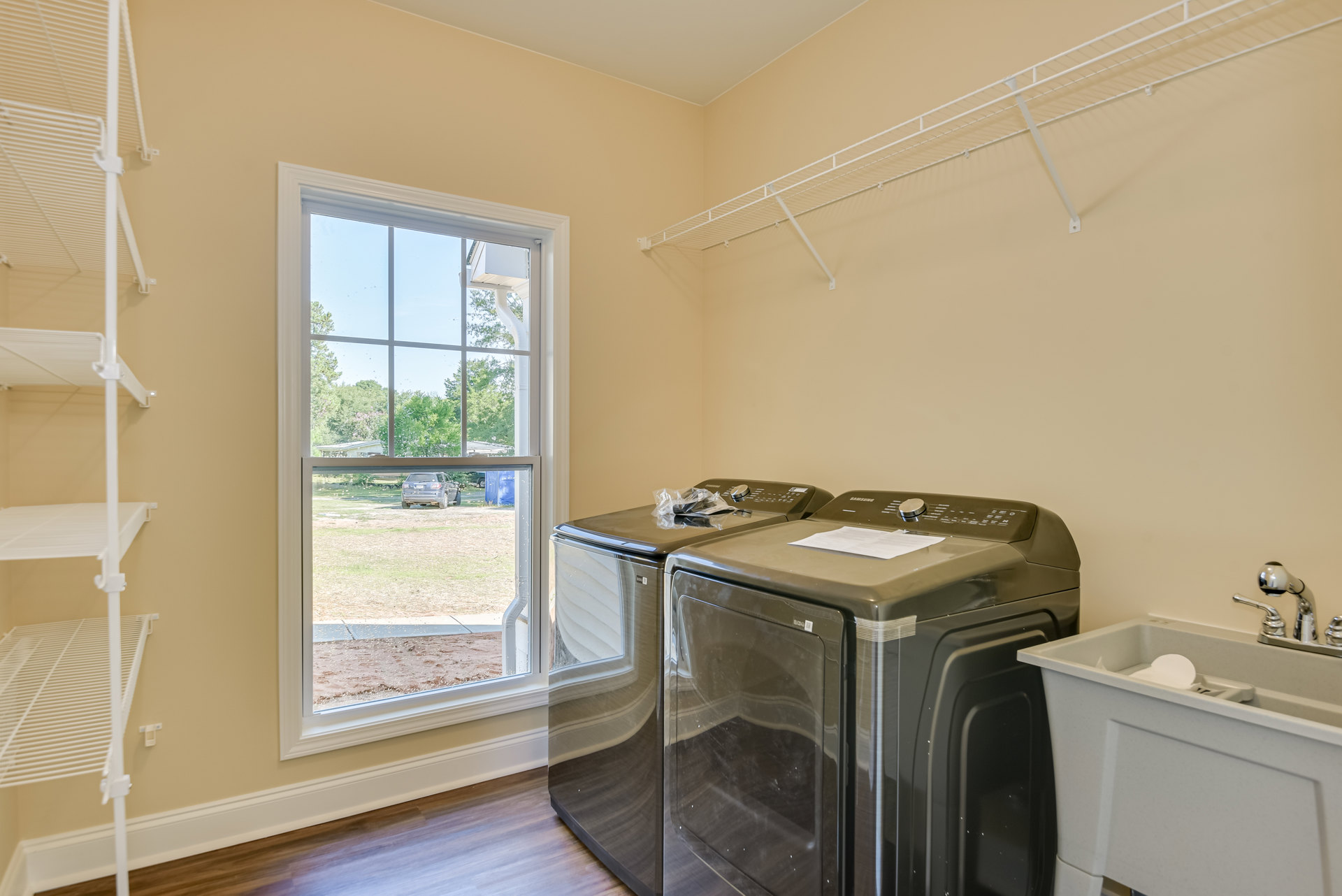 Laundry room with tile floor, white cabinetry, front-loading washer and dryer side by side, countertop with sink, tissue in basin, window overlooking parked car.