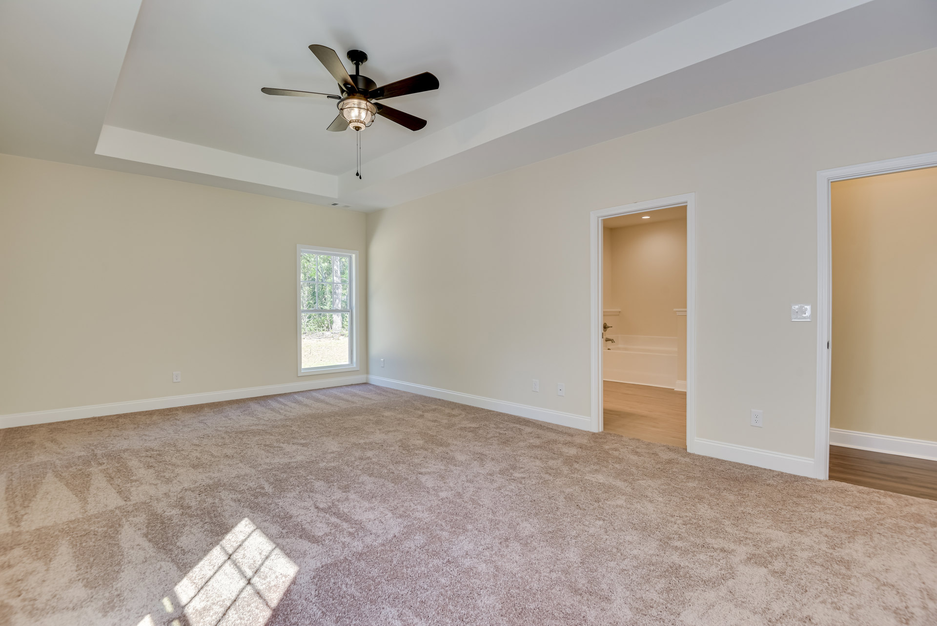 Carpeted room with white walls, ceiling fan with light fixture, large window showing trees outside