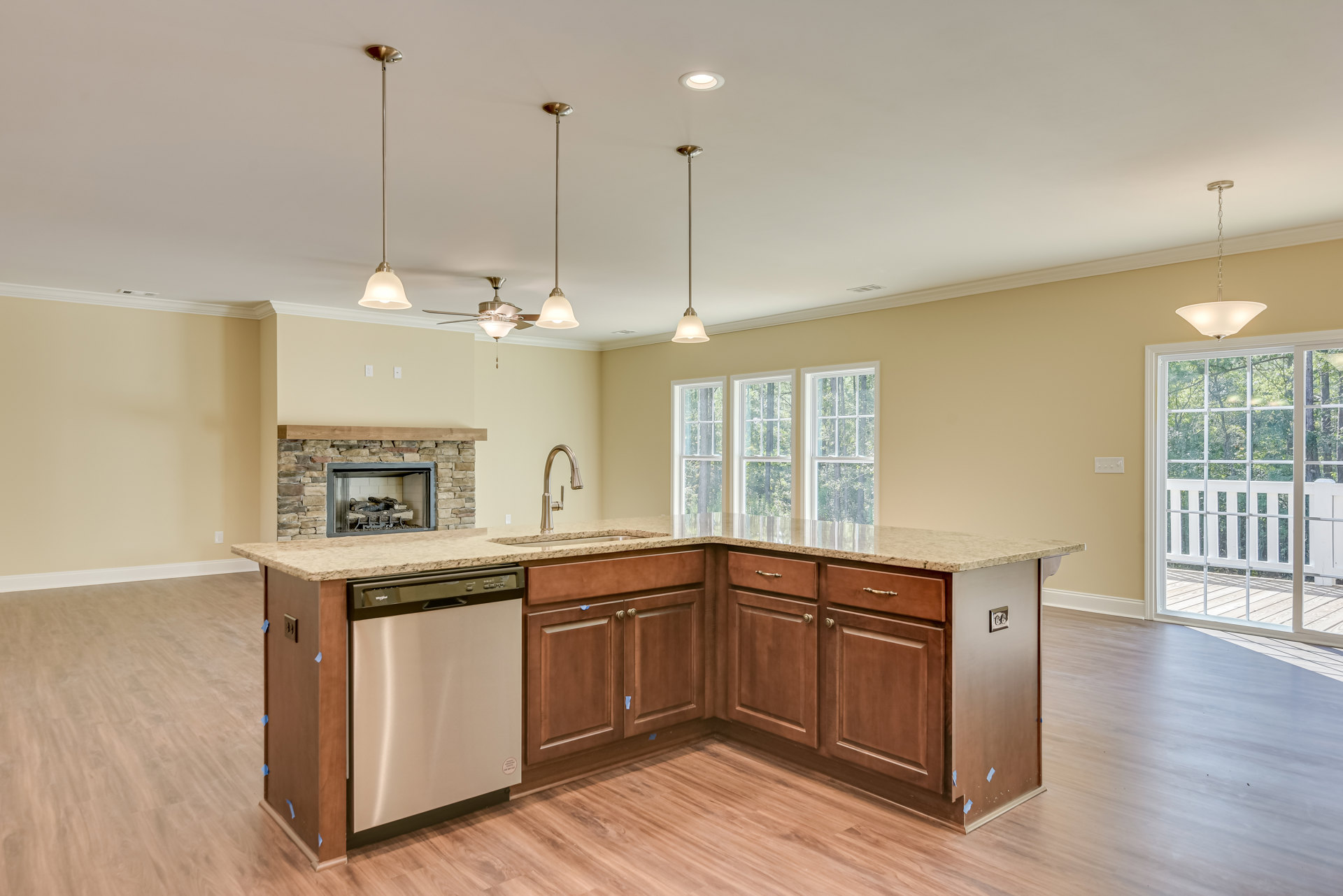 Open kitchen with wood cabinetry, stainless stove, white dishwasher on wood countertop, fireplace with stacked logs, window with white railing overlooking trees, light fixture and
