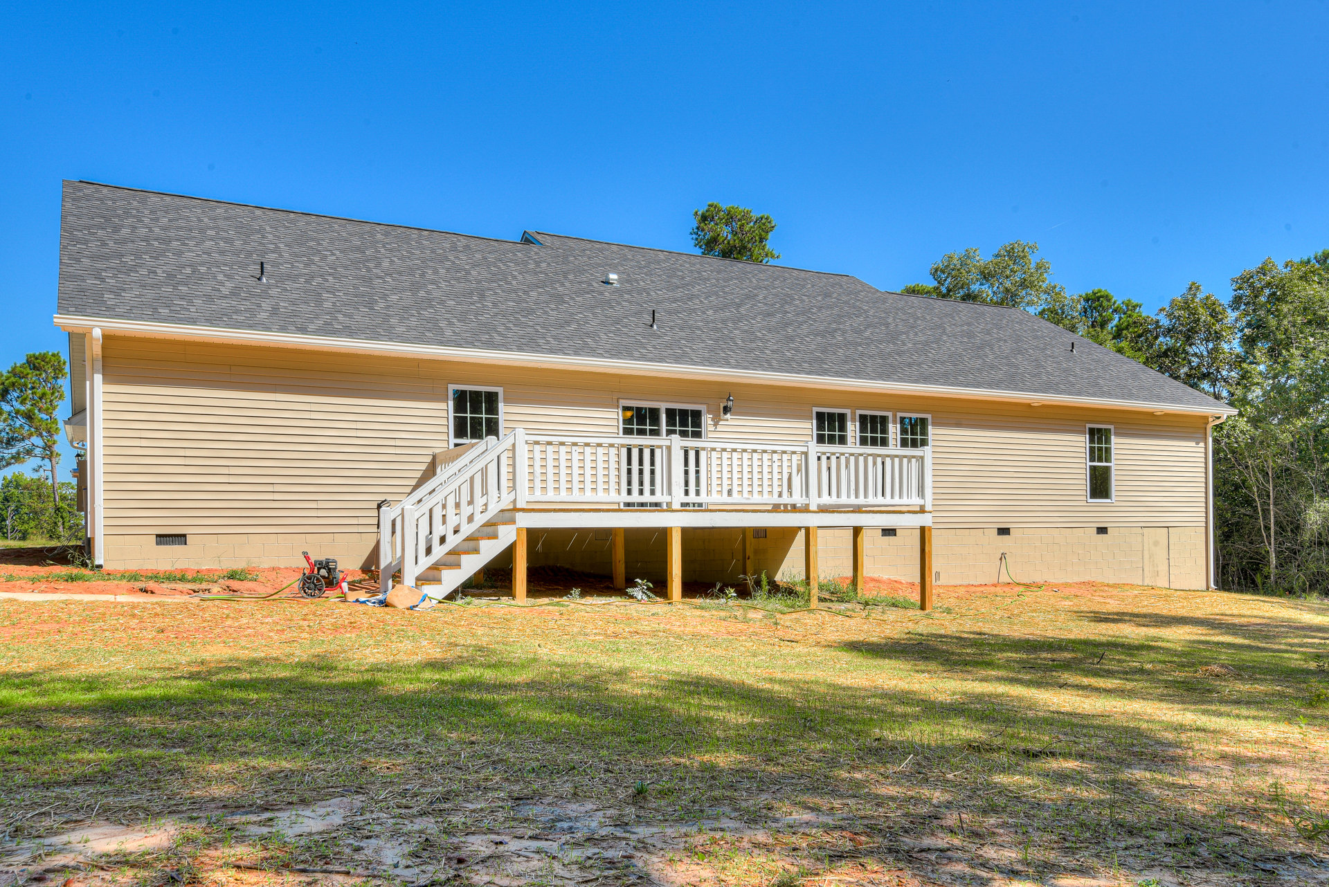 Two-story house with white deck and stairs overlooking grassy yard, white-trimmed windows, and mature tree near roofline
