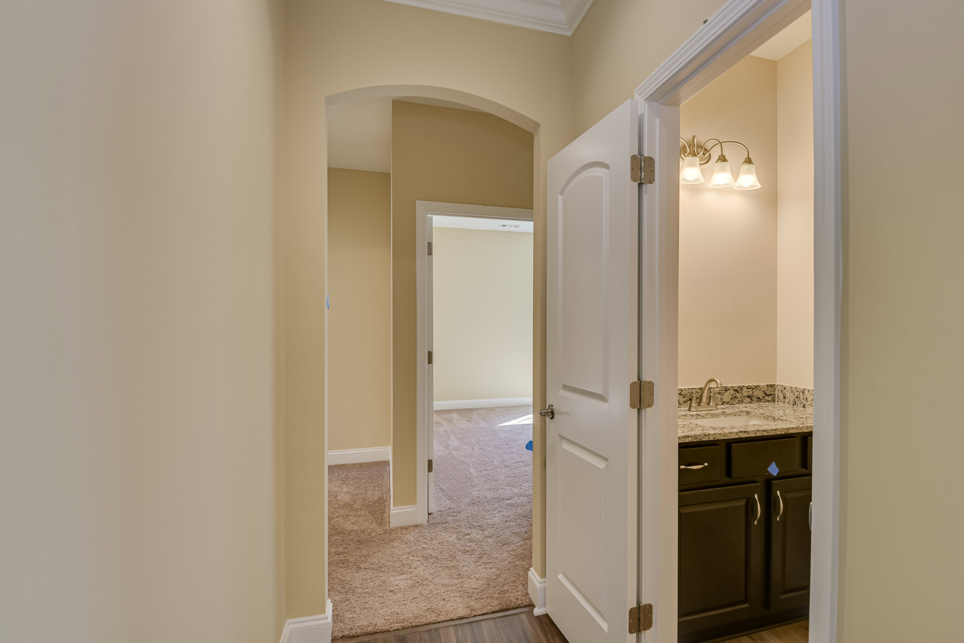 Hallway with carpeted floor and white trim, white door, black cabinet with silver handles and blue sticky note, wall-mounted sink, three-light fixture, white walls with metal frame