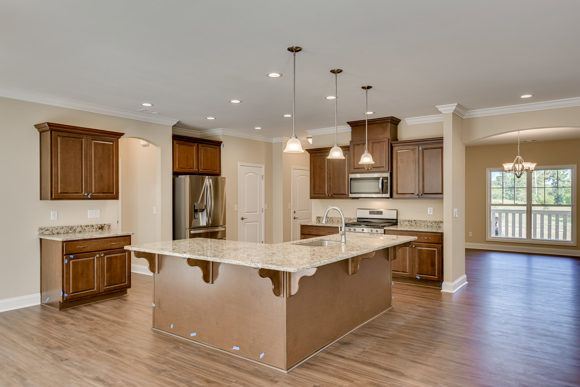 Spacious kitchen featuring a large granite island, stainless steel refrigerator with water dispenser, open microwave oven, hardwood floors, white cabinetry, and a window with a