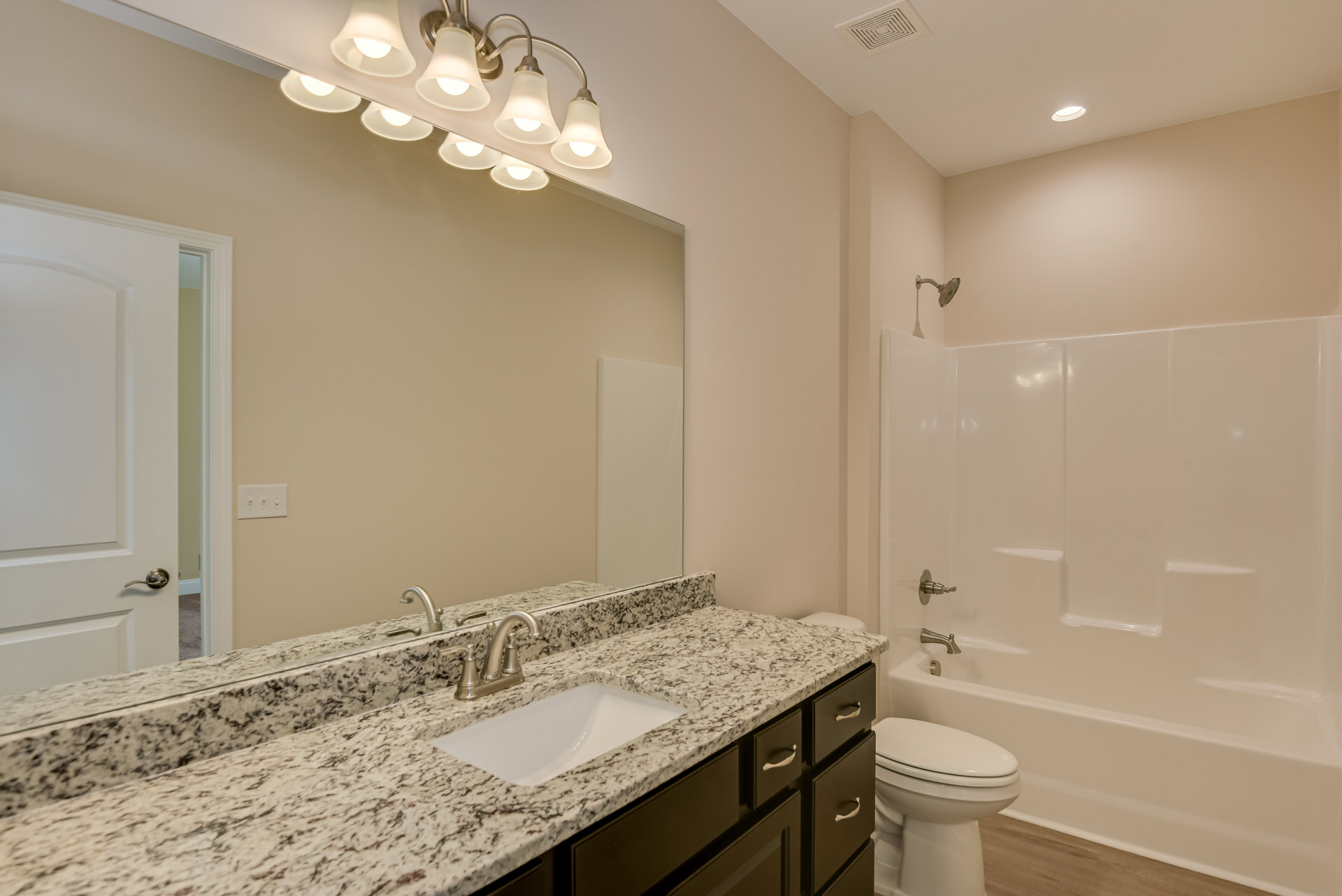 Bathroom with marble countertop, white sink and silver faucet, white toilet with lid closed, wall-mounted group of lights, white cabinet below sink, light tile flooring and neutral