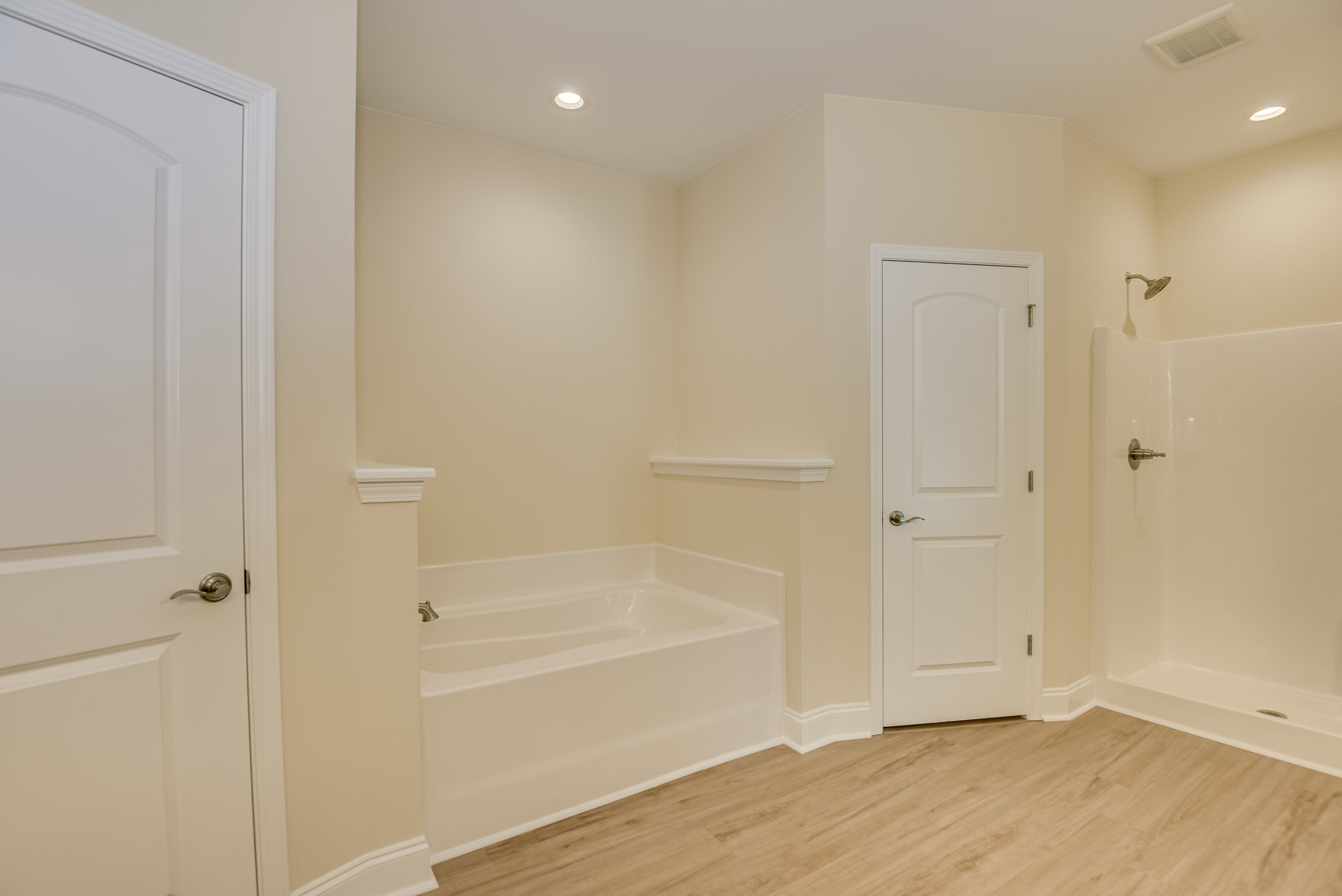 White bathtub with silver faucet set against tiled wall, adjacent to white door with chrome handle, light-colored flooring and cabinetry visible