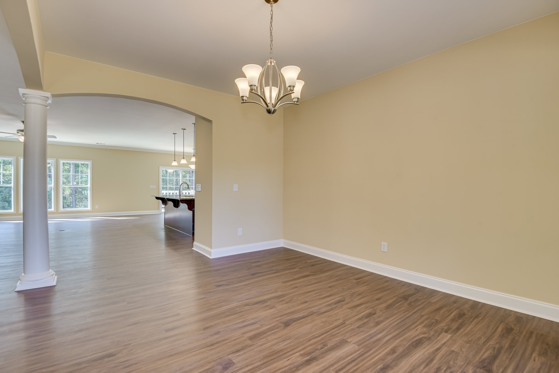 Wood floor with white baseboards, large window framed by white curtains, tree visible outside, ceiling-mounted chandelier with chain and lamps.