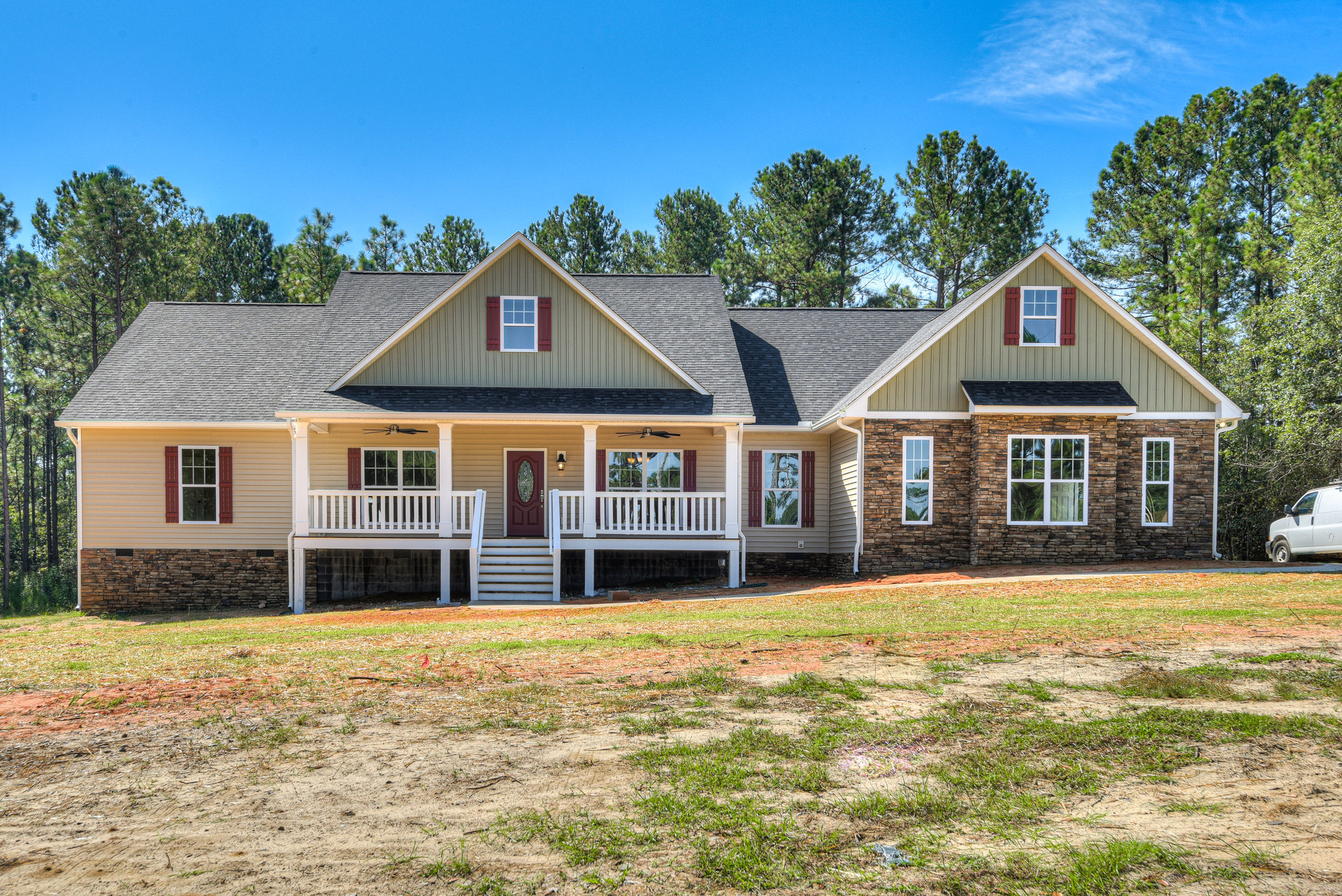 Two-story house with red front door, covered porch, white-framed windows, and grassy front yard bordered by trees.