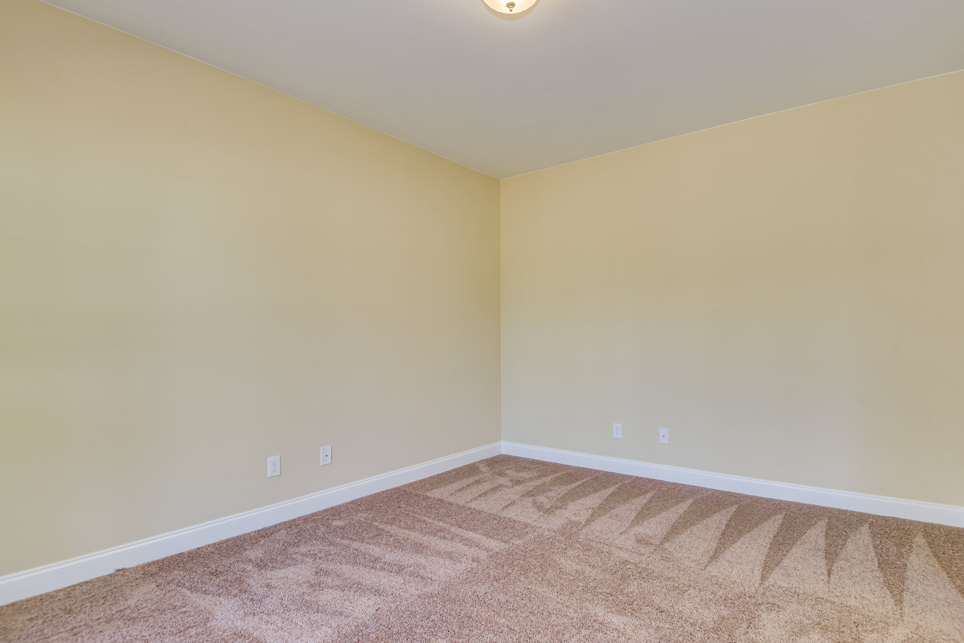 Spacious room with beige plaster walls, white ceiling molding, checkered carpet flooring, and modern ceiling light fixture