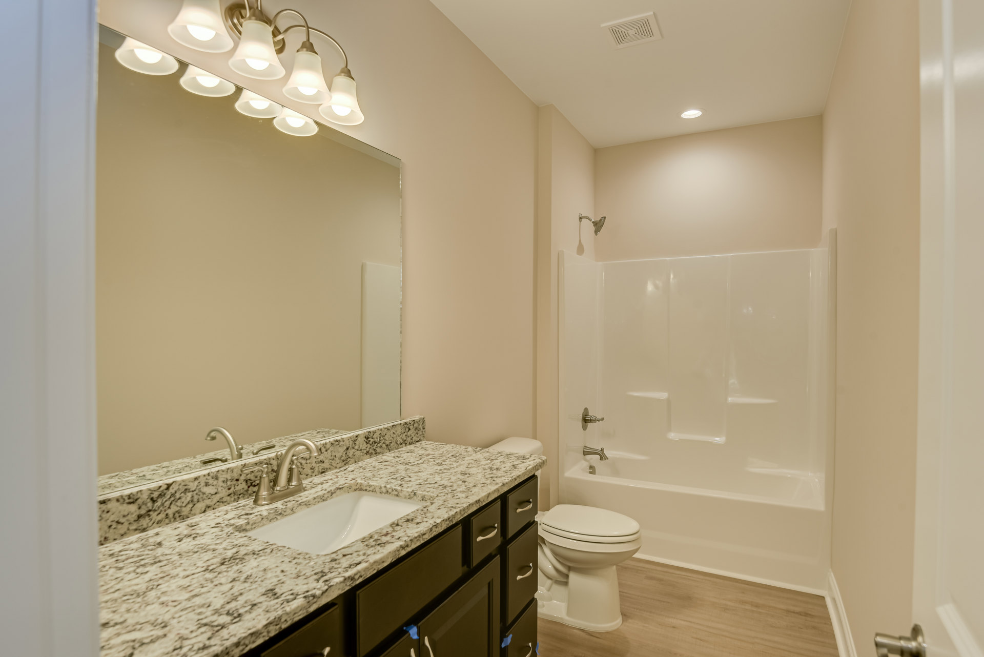 Bathroom with white bathtub, marble countertop sink, white toilet, wall-mounted mirror with multiple lights, light tile flooring and neutral walls