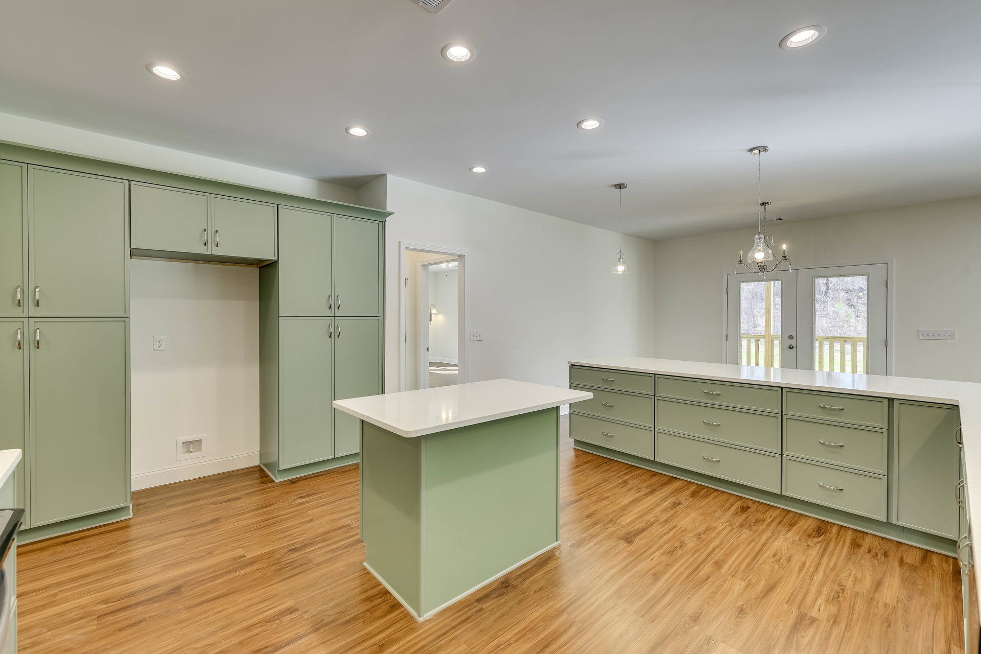 Kitchen with wood flooring, white island featuring a green countertop, white cabinetry, tile backsplash, ceiling light fixture, and white wall with electrical outlet
