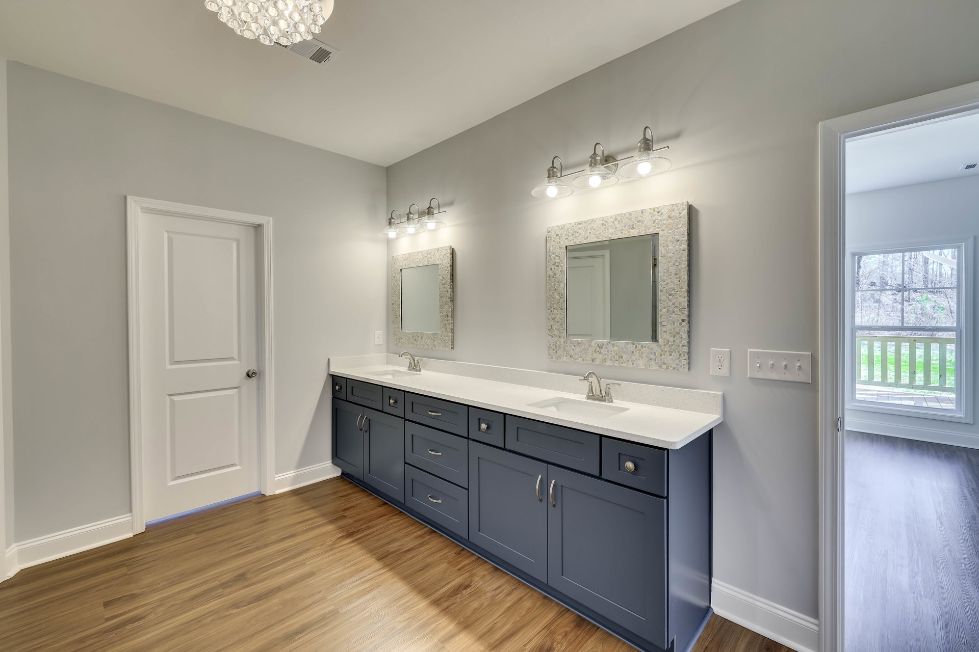Bathroom with dual sinks, blue and white countertops, large wall-mounted mirror with white frame, white cabinetry, silver faucet fixtures, white door with silver knob, light tile