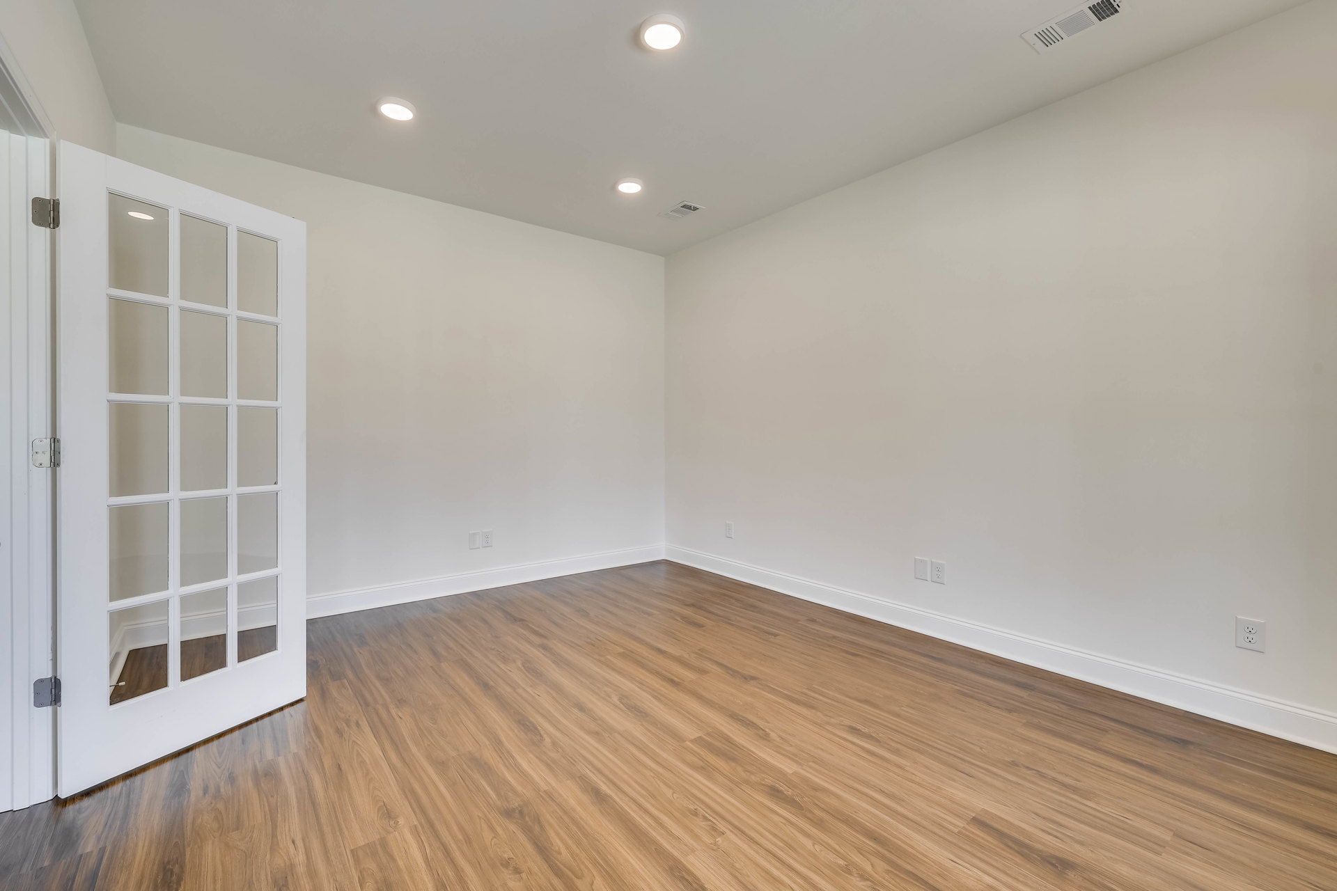 White walls and wood laminate flooring, ceiling light fixture, white door with glass panes