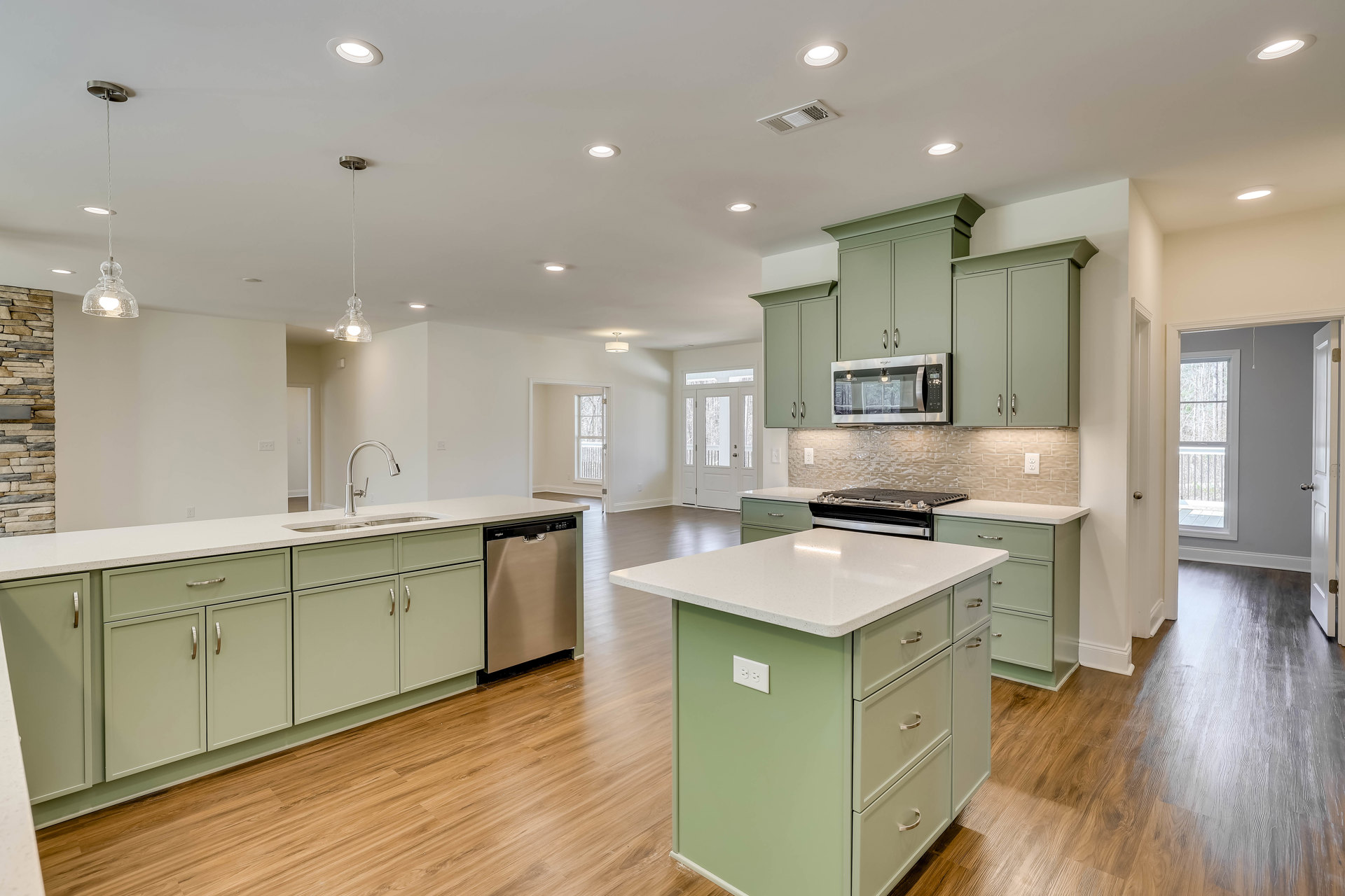 Green kitchen cabinets with wood flooring, kitchen island featuring drawers and a stove, built-in microwave illuminated, pendant light fixture hanging from ceiling, silver metal