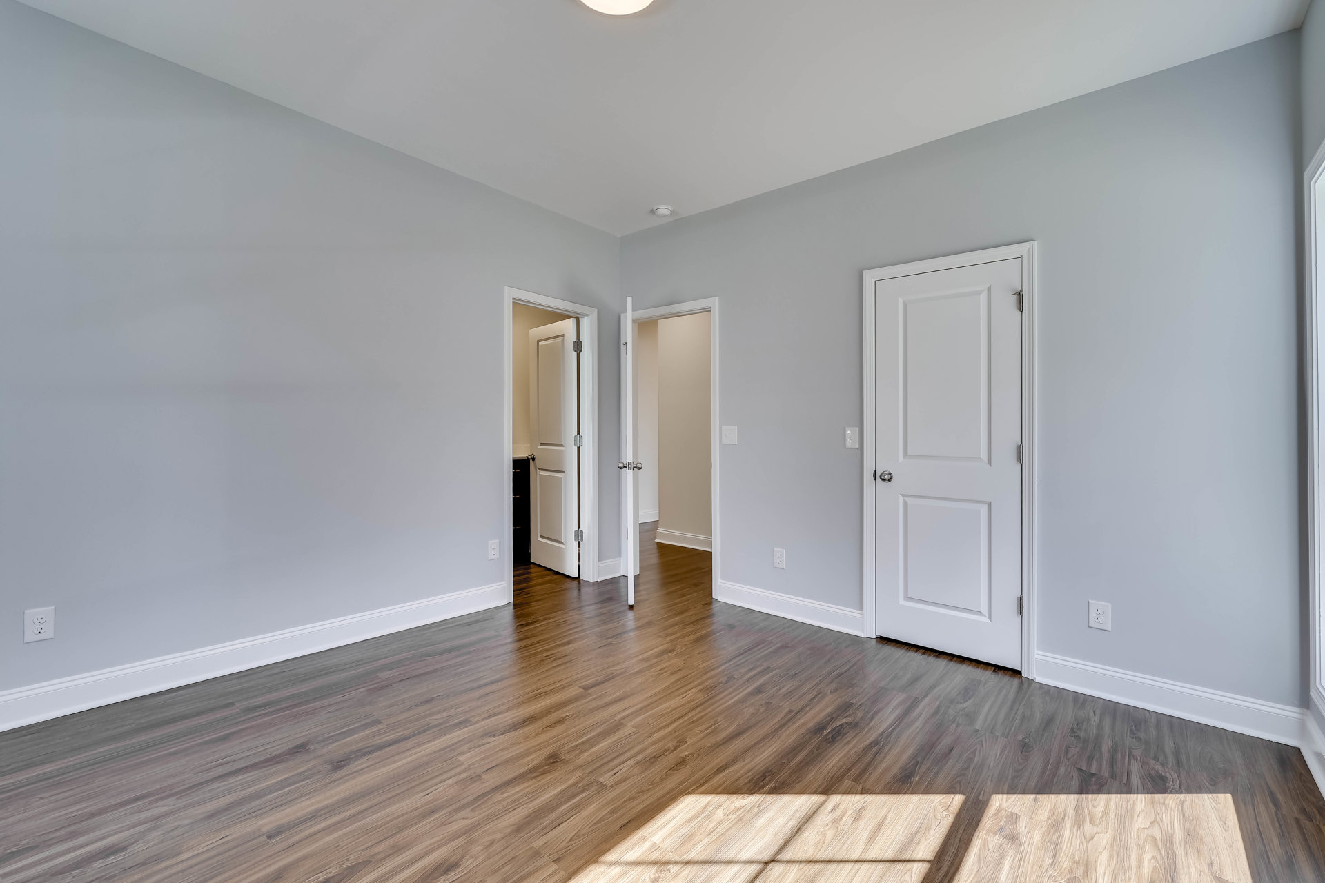 White paneled door with silver knob, wood flooring, white walls, and simple baseboards in a bright interior room
