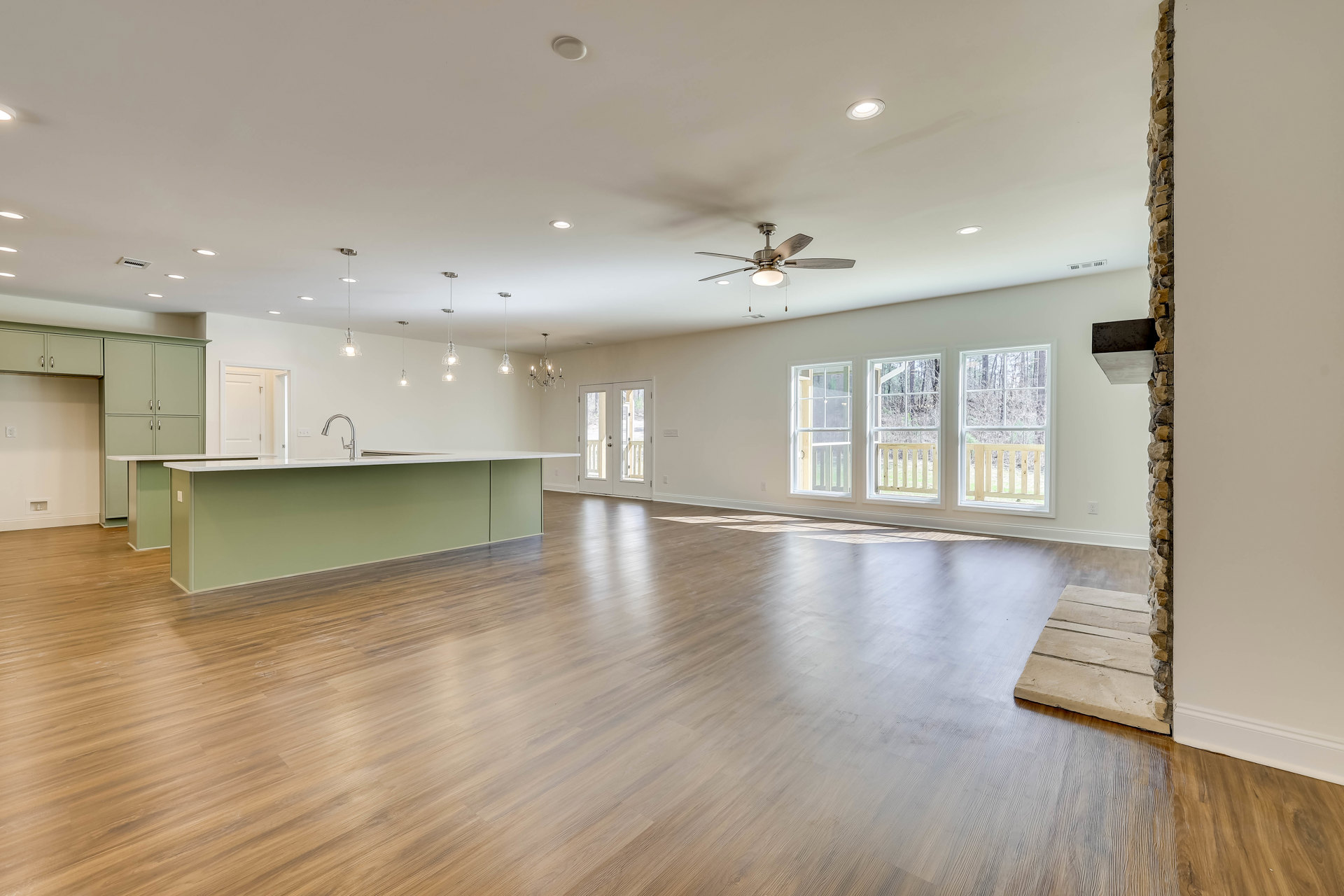 Open-concept kitchen with hardwood flooring, white cabinetry, stone countertops, stainless steel faucet, glass-paneled door, window overlooking trees, and black wall sign