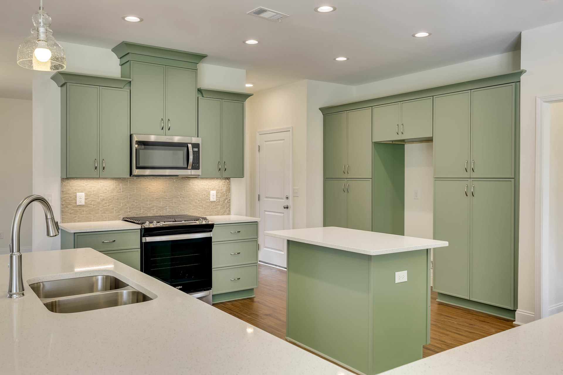 Green kitchen cabinets with stainless steel sink, open microwave, stove, white countertop island, tile backsplash, and ceiling light bulb