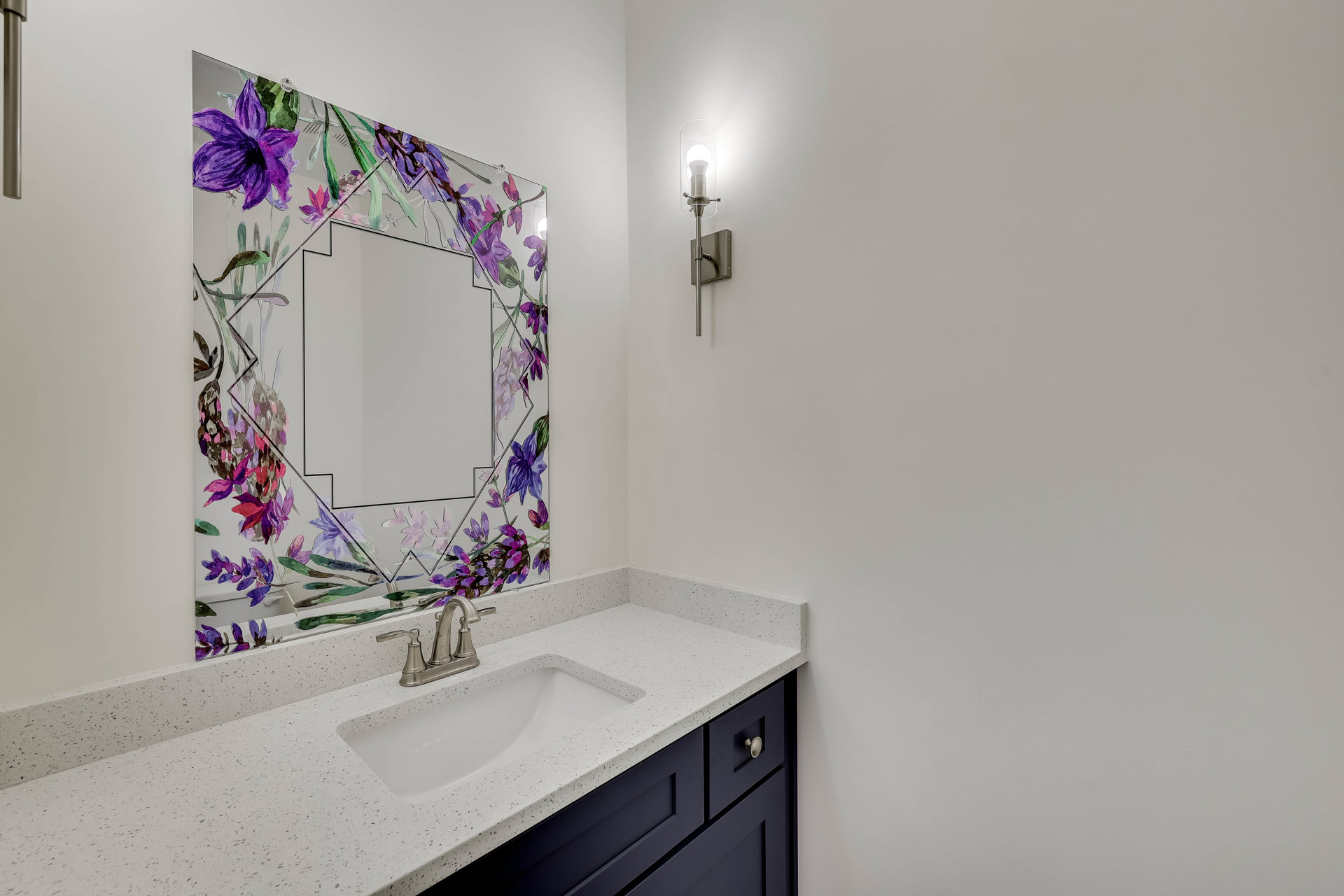 White bathroom vanity with silver faucet, rectangular mirror above, purple flower arrangement in glass vase on countertop, light wood cabinetry, neutral wall color